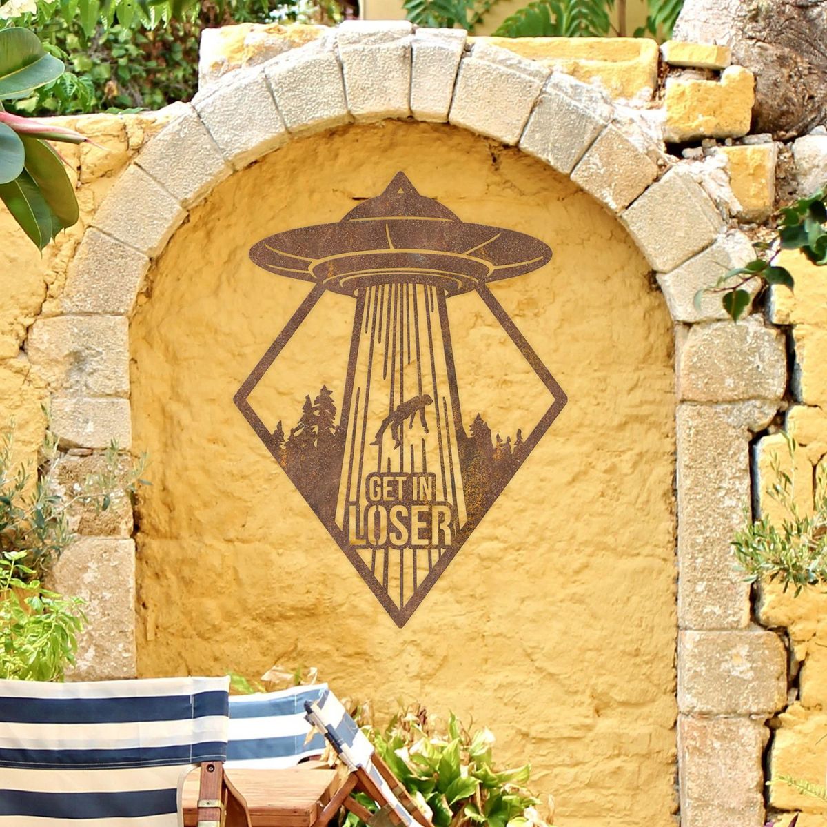 "Get in Loser" Alien Wall Art on a Yellow Brick Wall in the Garden