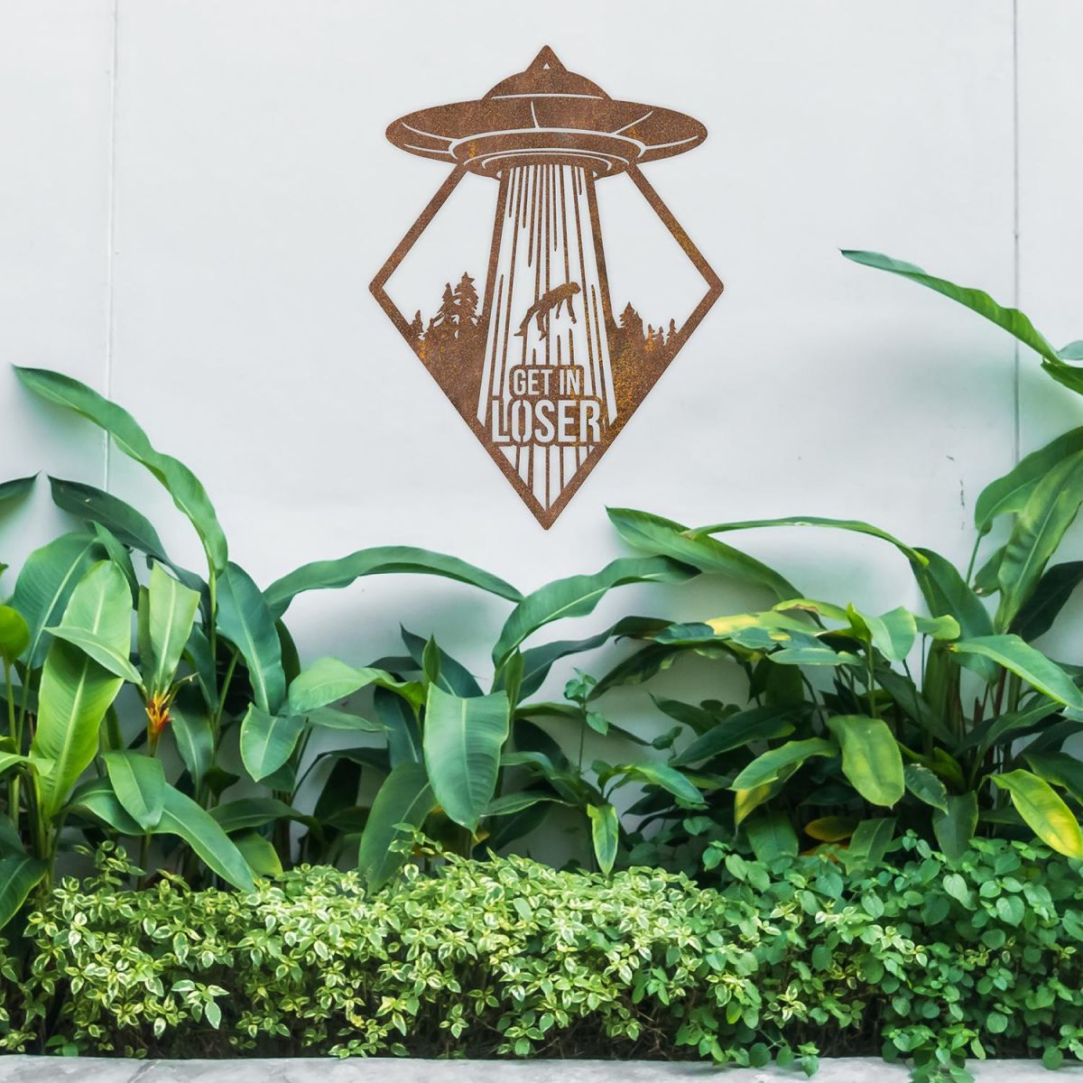 "Get in Loser" Alien Wall Art Above a Bush Outdoors