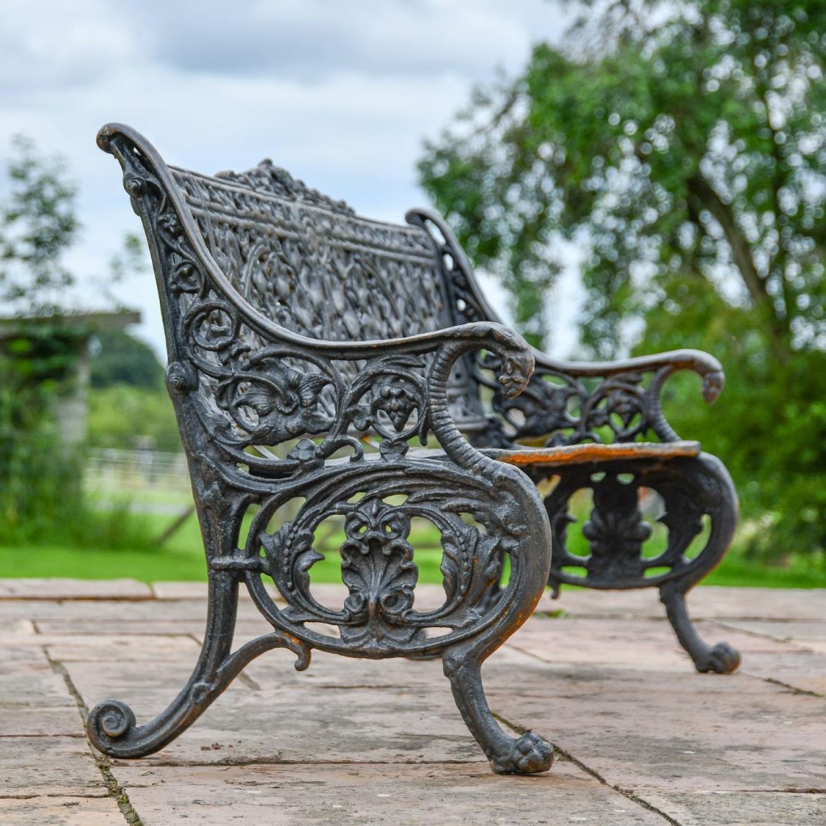 Side view of ornate detailing on scroll leaf aged black garden bench Side view of ornate detailing on scroll leaf aged black garden bench