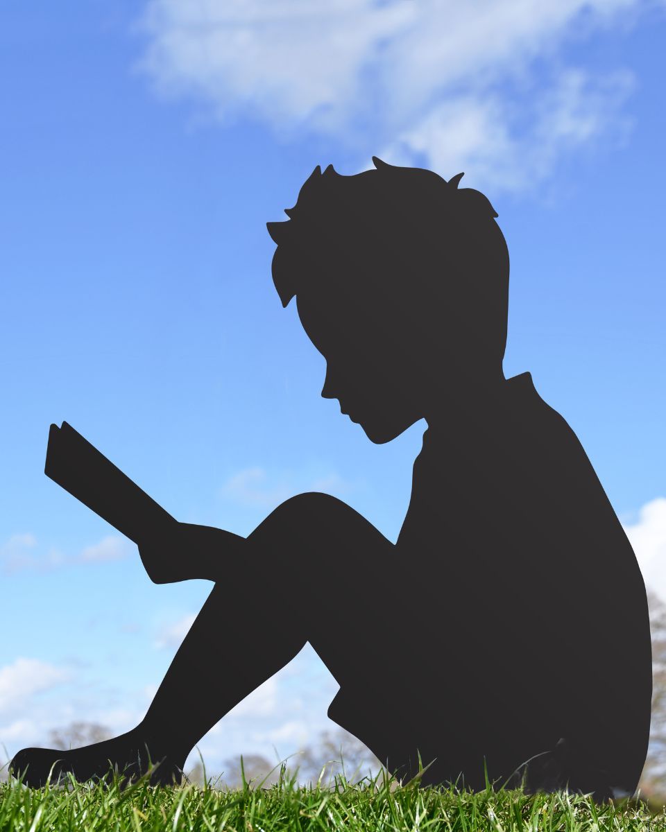 Boy With Book Silhouette sitting on grass with blue sky background 