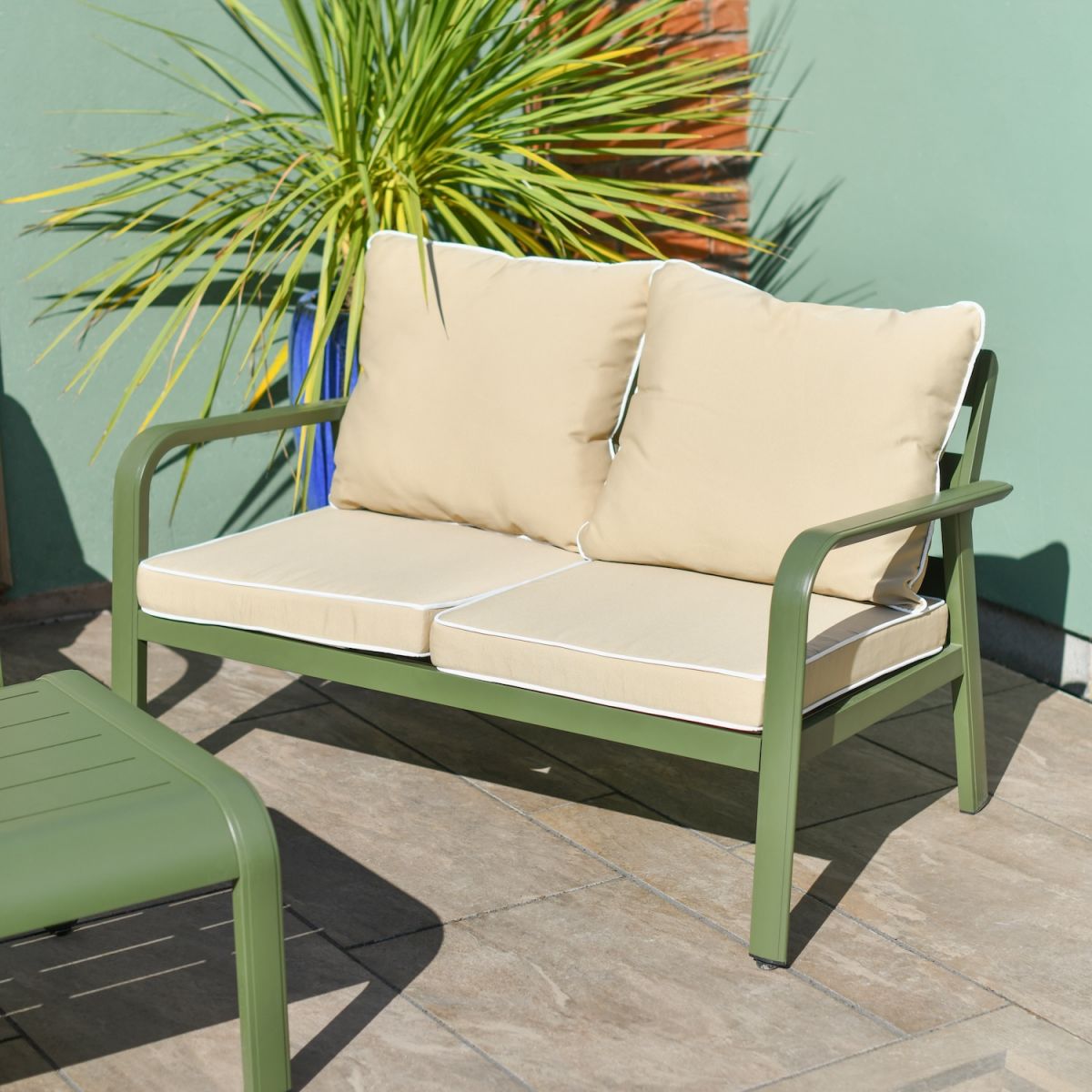 Close up of two seater sofa with cream cushions on modern green outdoor lounge set