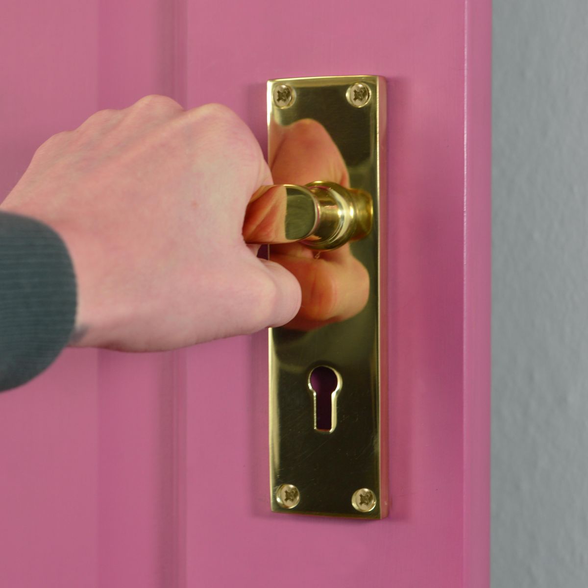Polished Brass Lever Handle With Key Hole on Pink Door in Use