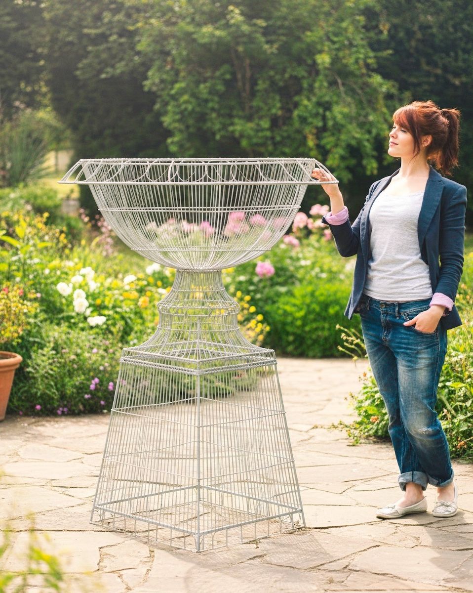 Digital illustration of St Austell Wirework Planter with lady stood next to planter admiring the frame set in a rustic garden scene