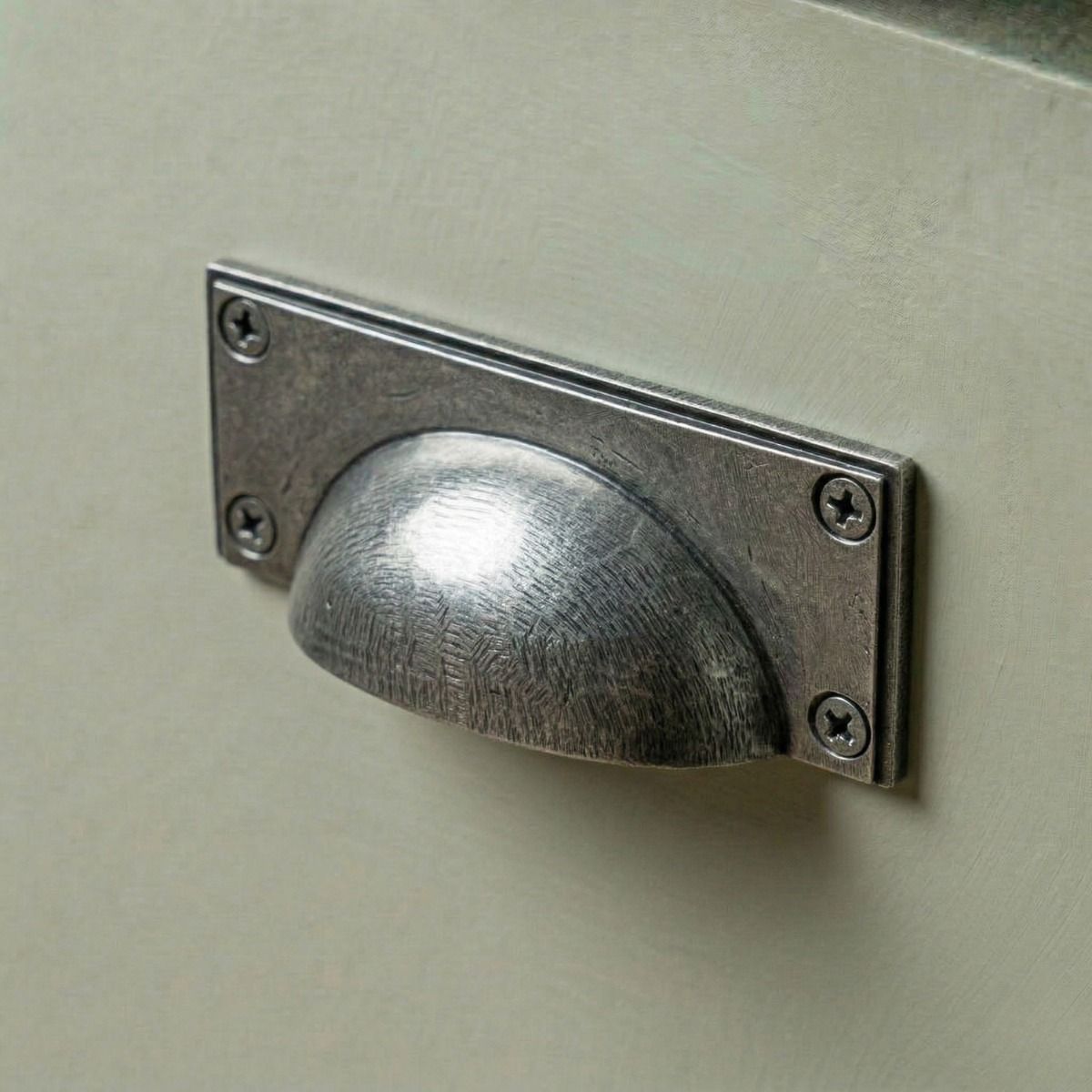 Digital Illustration of the Aged Pewter Rectangular Drawer Pull with Curved Handle Mounted on a Sage Green Cupboard Door.