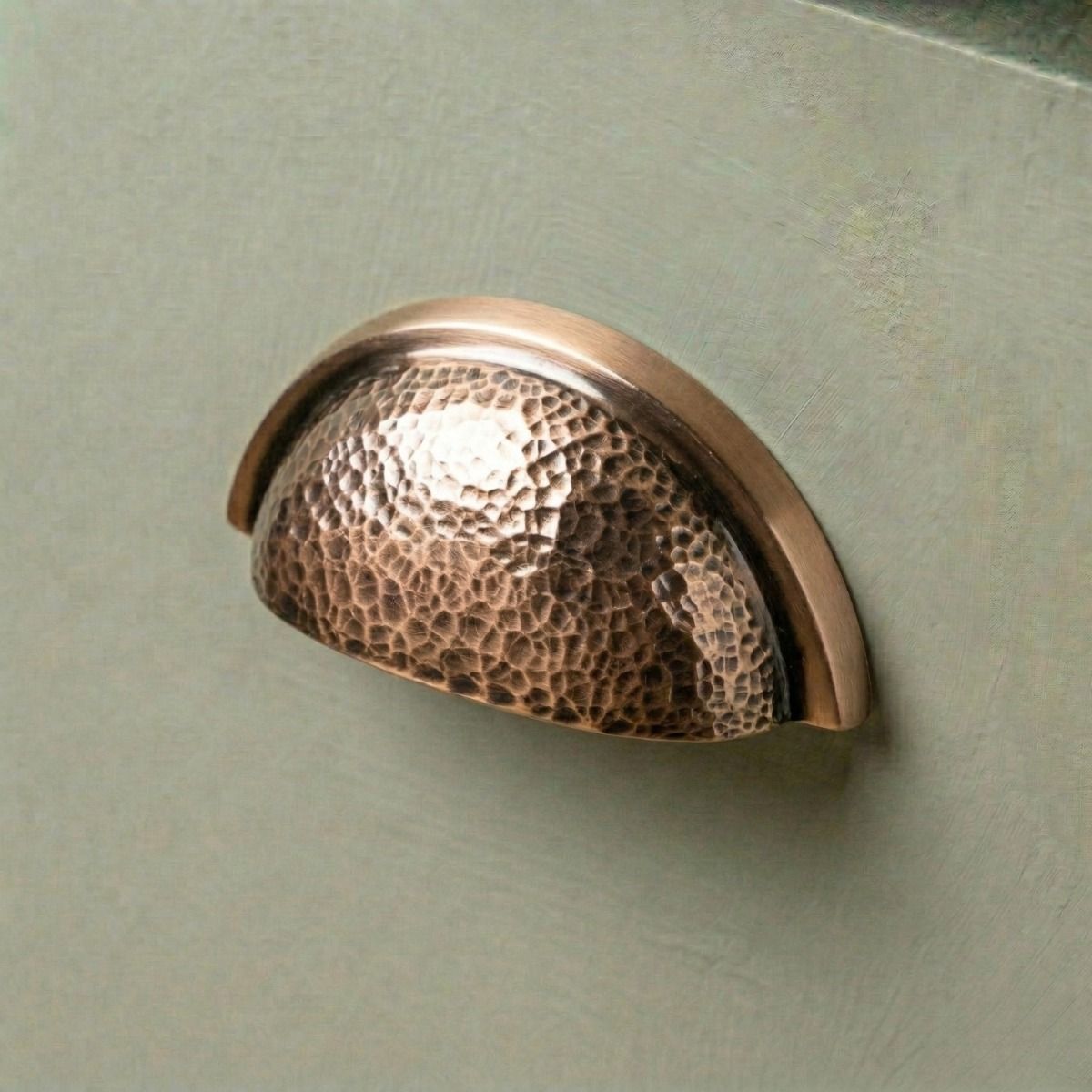 Digital Illustration of the Polished Copper Curved Drawer Pull with Hammered Handle Mounted on a Sage Green Cupboard