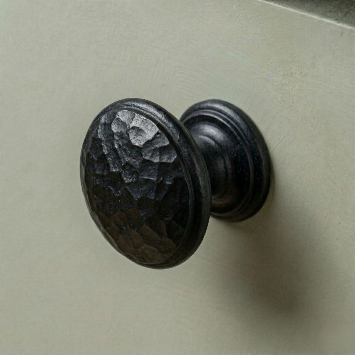 Digital Illustration of the Small Beeswax Beaten Iron Cupboard Knob Mounted on a Sage Green Cupboard
