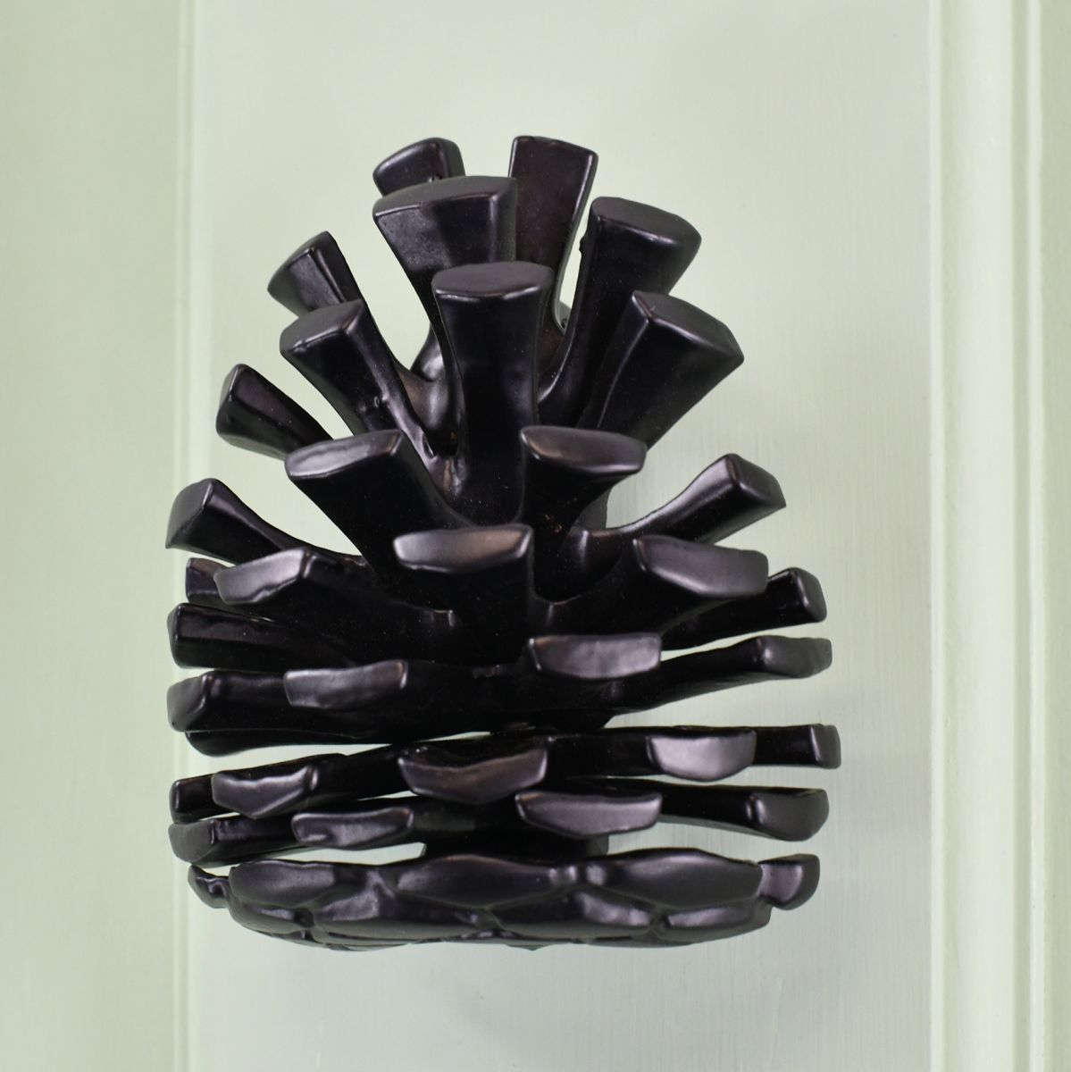 Black pine cone door knocker on pastel green door