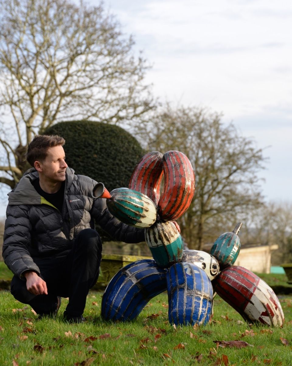 ‘Tangle’ the Balloon Dog Upcycled Oil Drum Garden Sculpture with man crouched down next to sculpture for scale