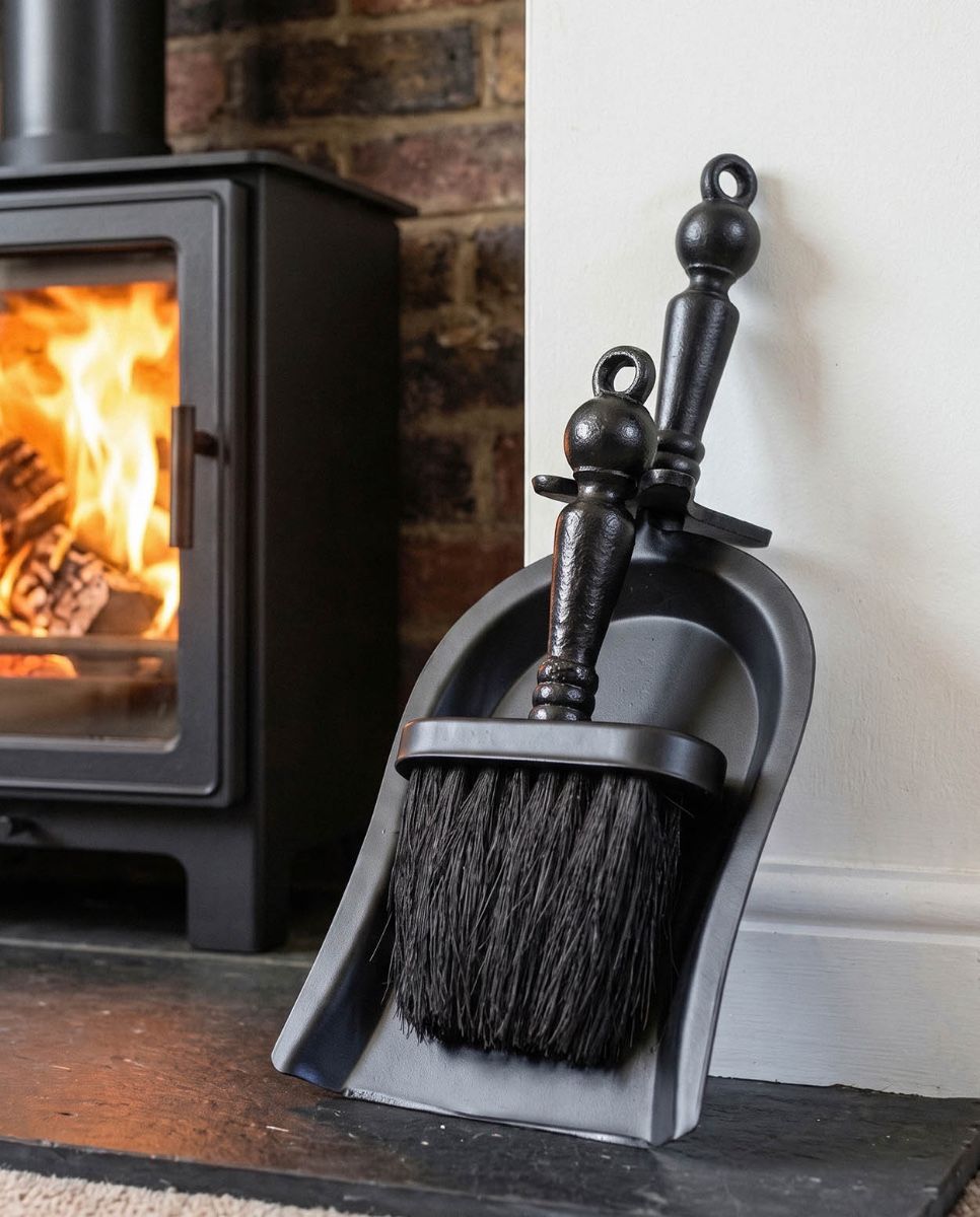The "Duchess" Black Iron Shovel and Brush Set next to some Logs ready for use in a Log Burner Stove - Digital Illustration