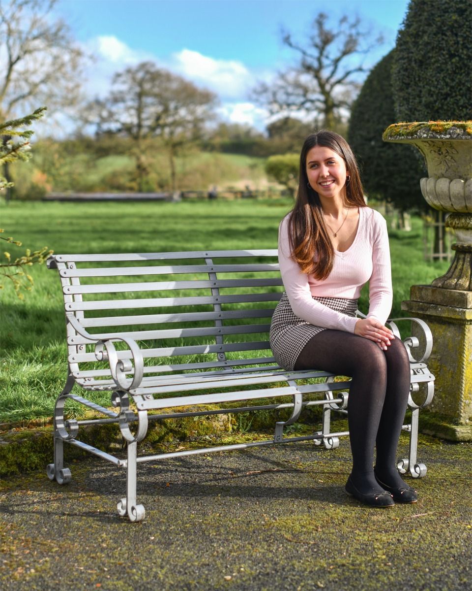 Grey Two Seater Park Bench With woman Sat on it 