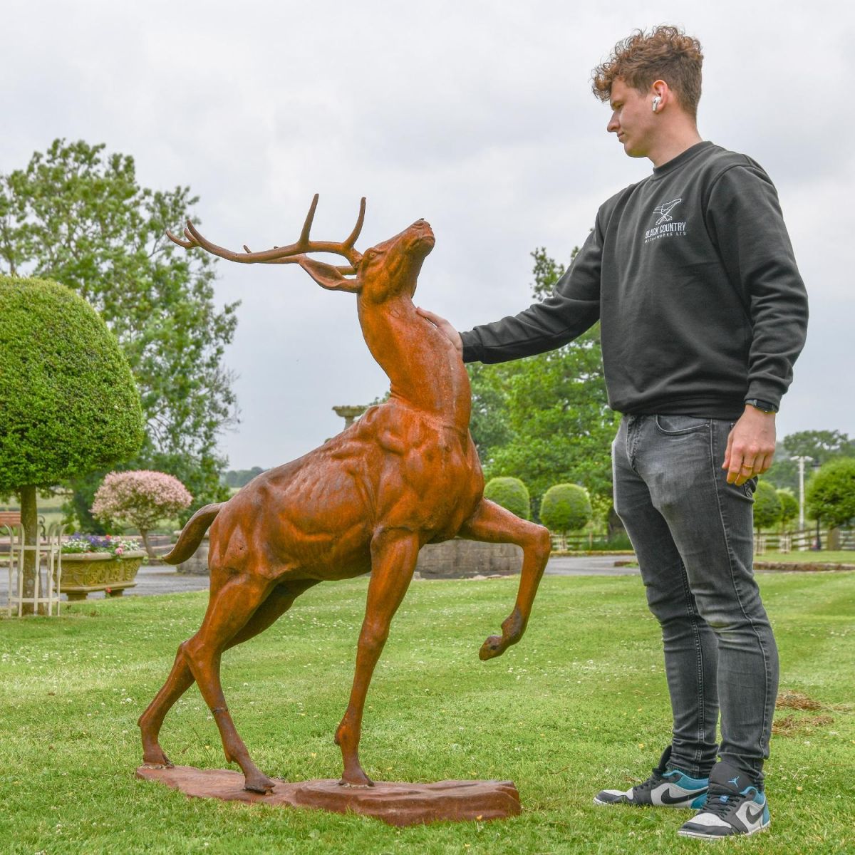 Male standing next to proud stag sculpture 