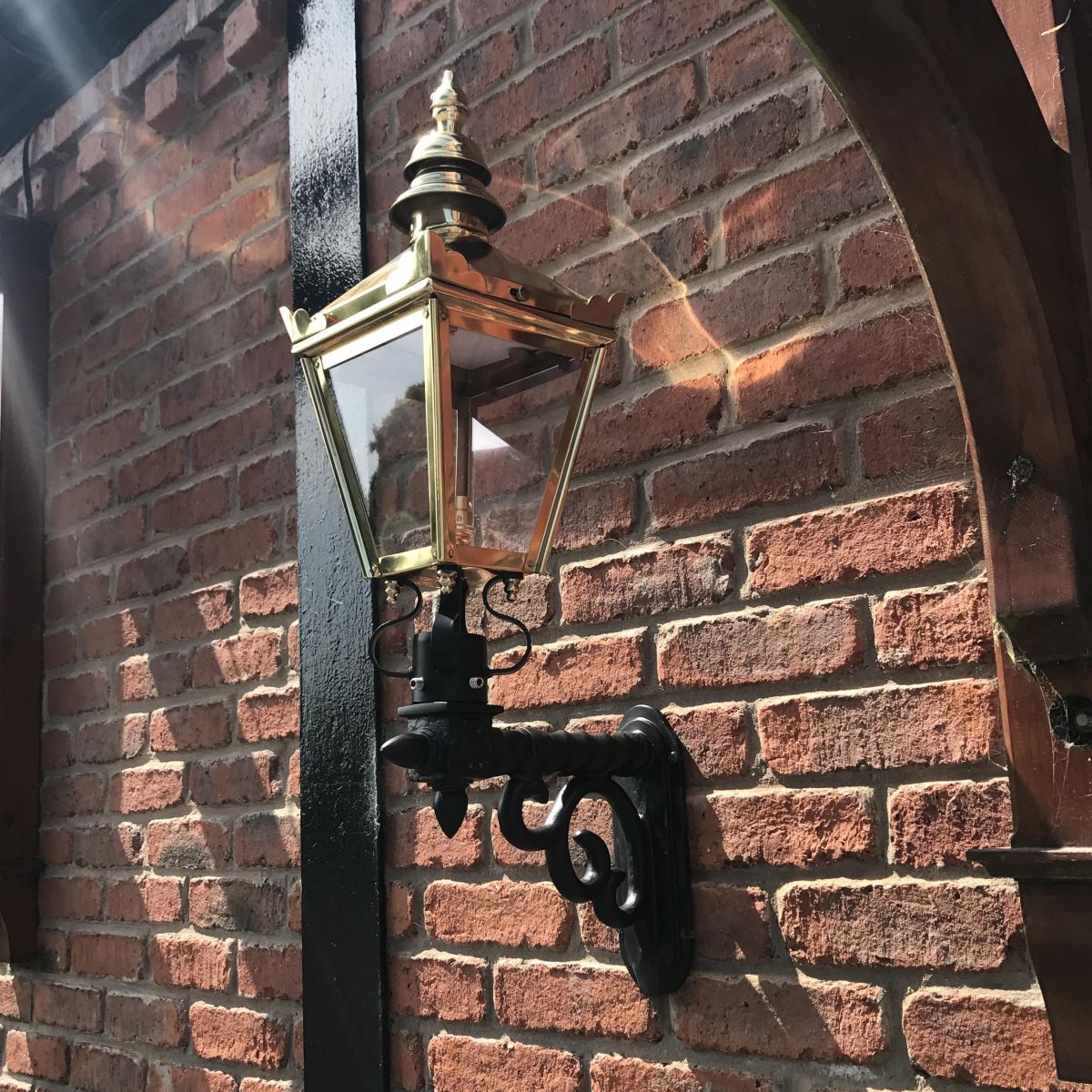 Polished Brass Harrogate Wall Lantern on Bracket Mounted on a Brick Wall in the Garden