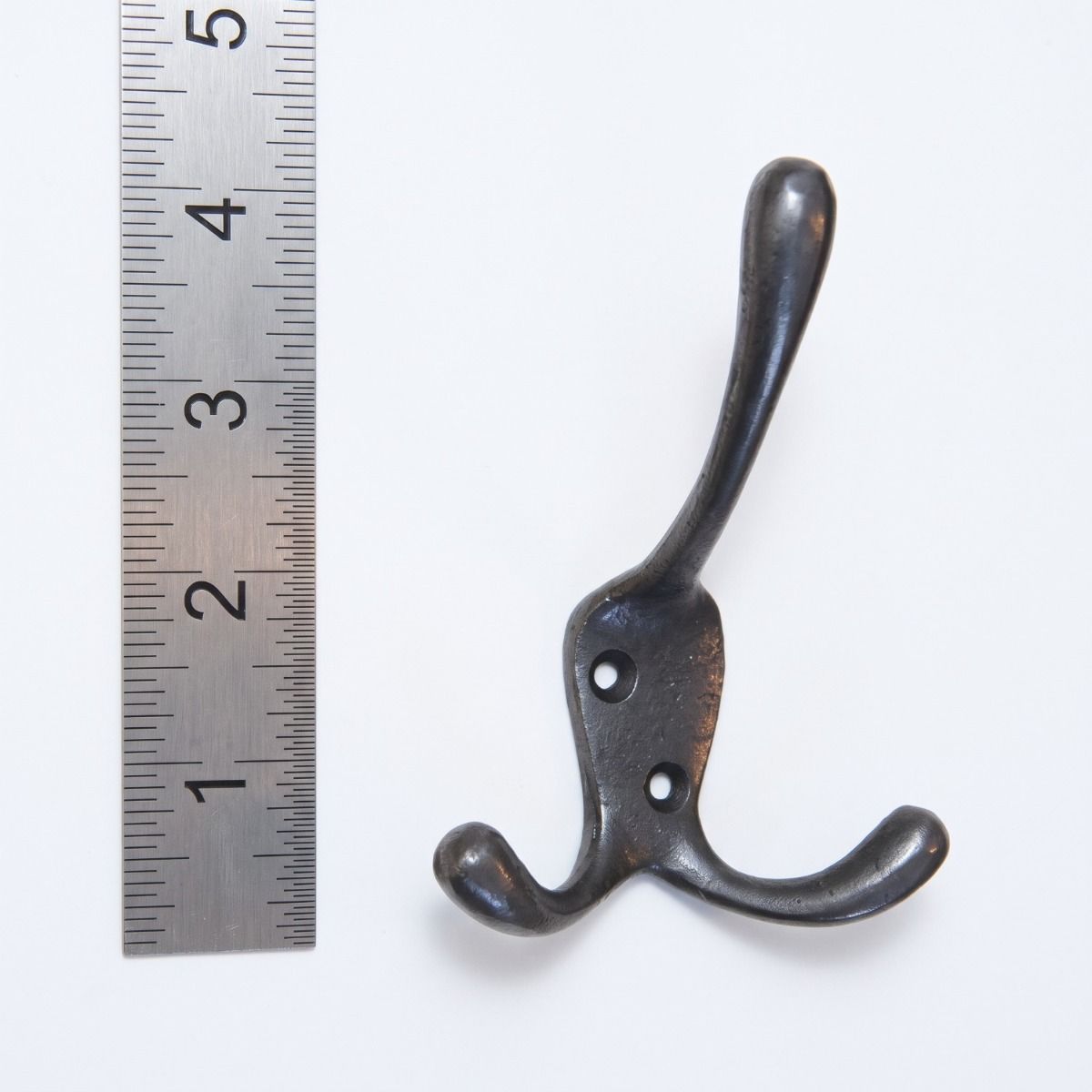 The Blacksmith Vintage Cast Iron Three-Prong Hall Hook - 100mm On a White Background  next to a Ruler - Digital Illustration