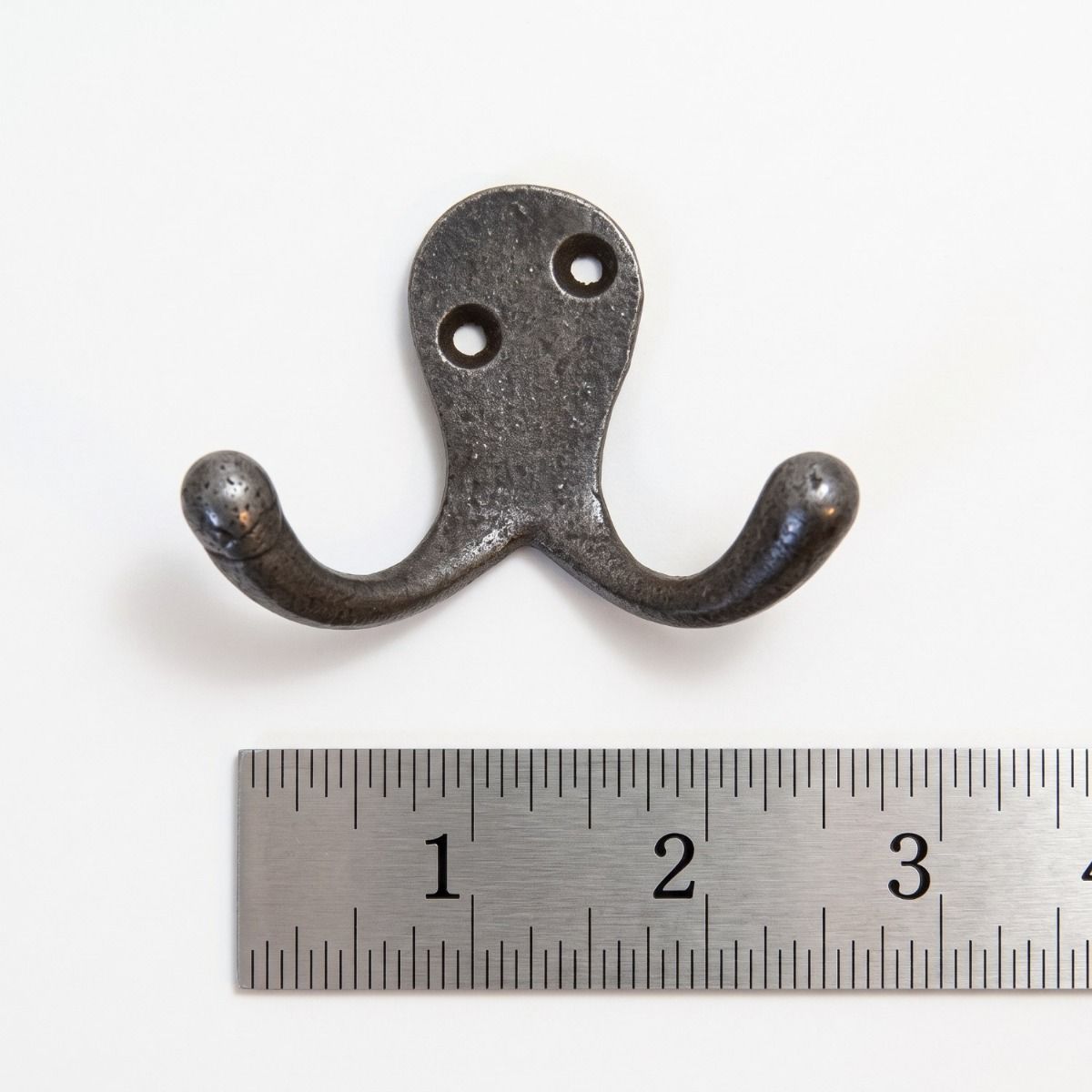 The Cotswold Double Ball-Tip Cast Iron Hook on a White Background next to a Steel Ruler for Scale - Digital Illustration