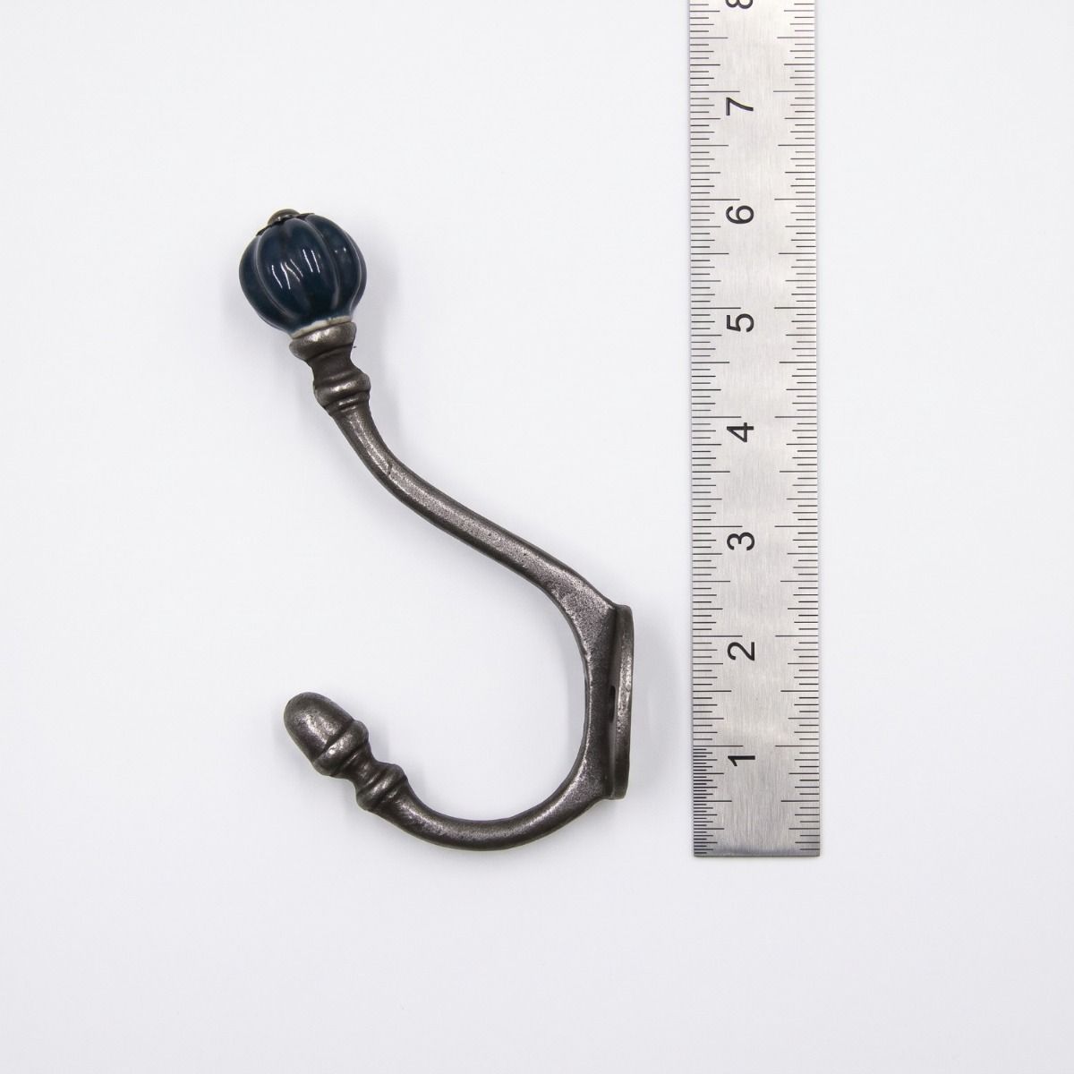The Ironmonger Acorn Dark Green Ceramic Coat Hook - 125mm on a White Background next to a Steel Ruler for Scale - Digital Illustration