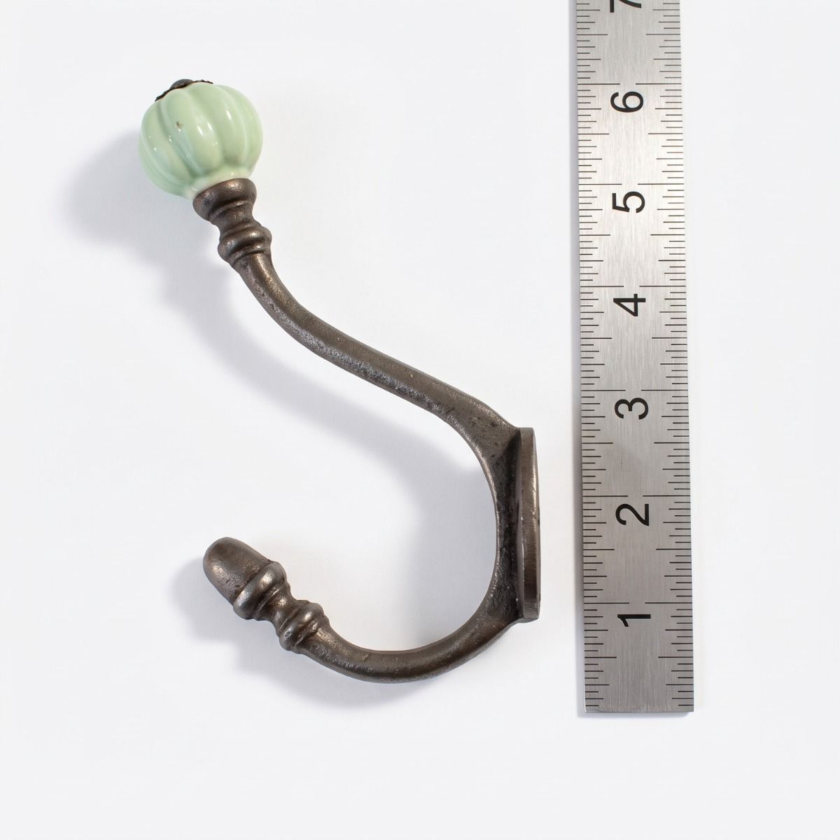 The Ironmonger Acorn Light Green Ceramic Coat Hook - 125mm on a White Background next to a Steel Ruler for Scale - Digital Illustration