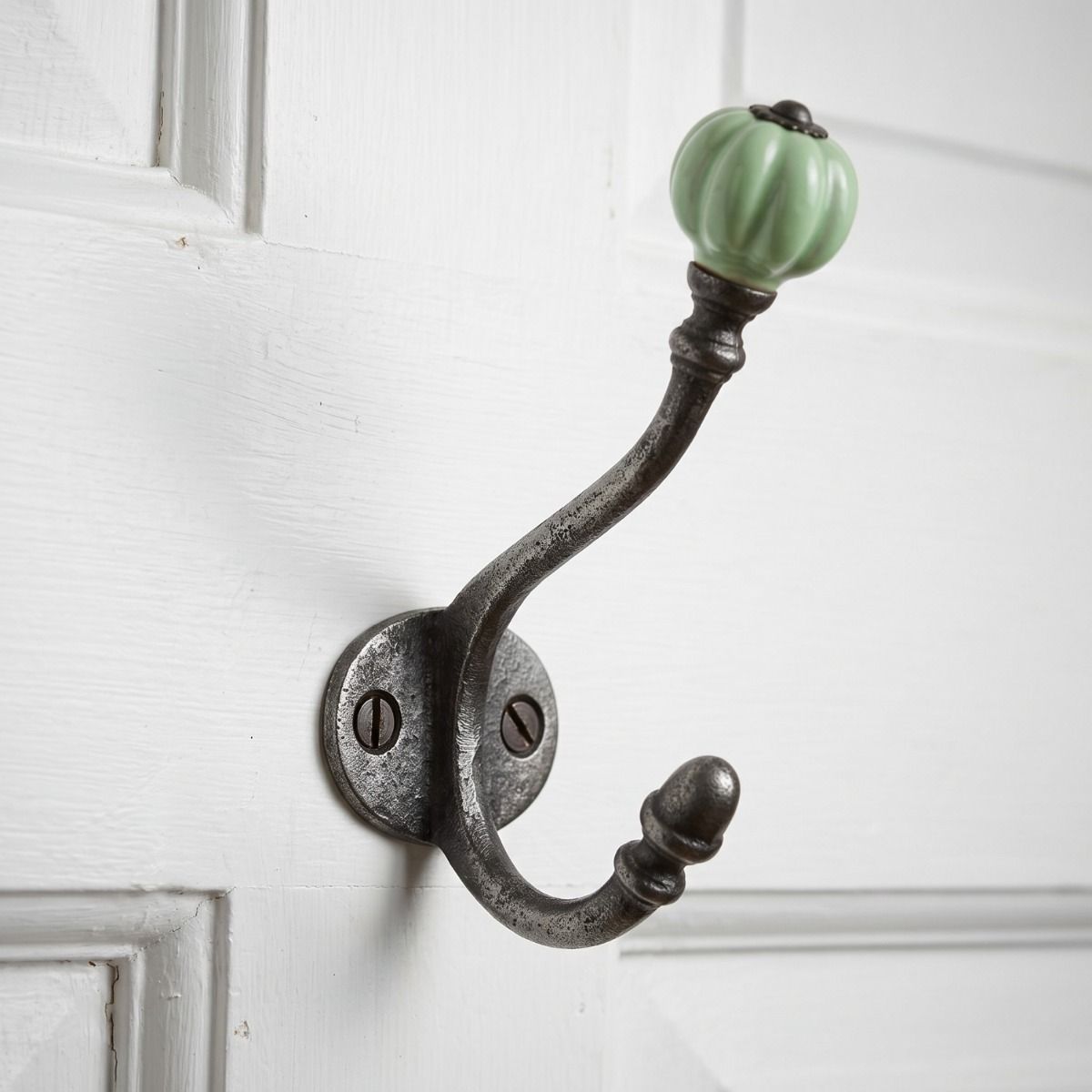 The Ironmonger Acorn Light Green Ceramic Coat Hook - 125mm Shown Mounted on the Back of a White Door - Digital Illustration