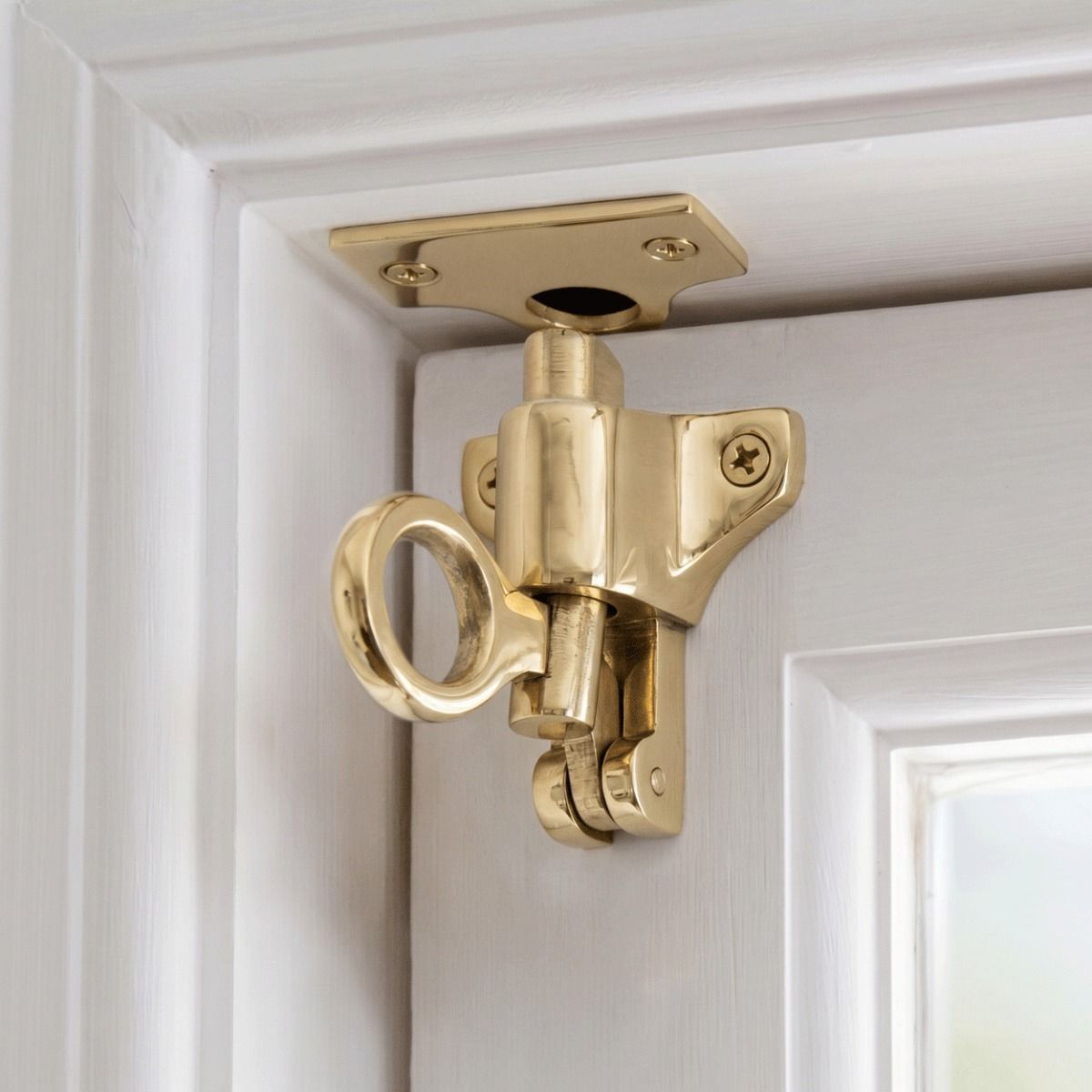 The "Atwood" Polished Brass Fanlight Catch with Two Keeps Attached to a White Door and Door Frame in a Contemporary Home Interior - Digital Illustration 