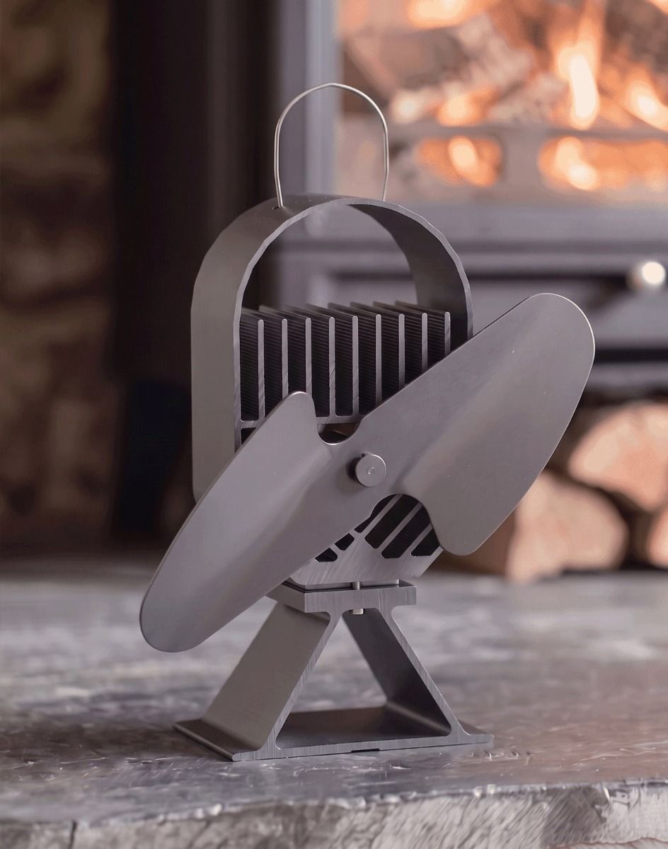 The 24cm Black "Air Deco" Eco Wood Stove Fan on na Black Stone Fireplace with a Log Burner in the Background - Digital Illustration