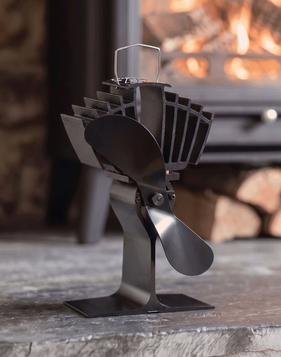 The 25cm Black "Air Max" Eco Wood Stove Fan on a Stone Hearth in Front of a Lit Log Burner Stove - Digital Illustration