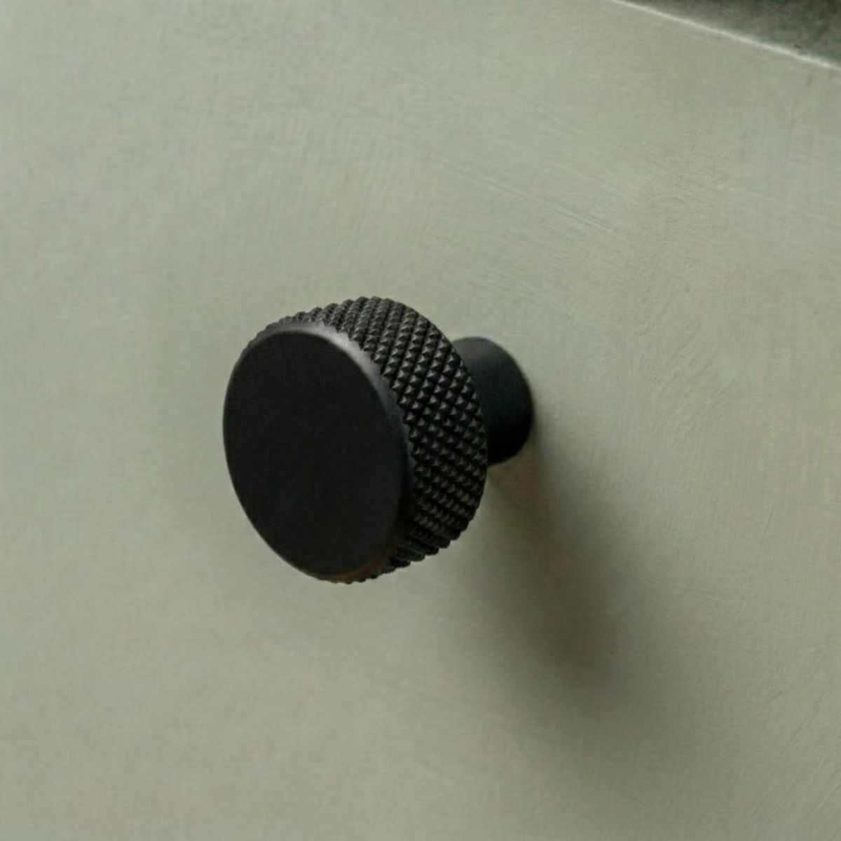 The 25mm "Vesper" Knurled Edge Cabinet Knob in Matt Black for Kitchen Cupboards Mounted on a Sage Green Drawer - Digital Illustration 