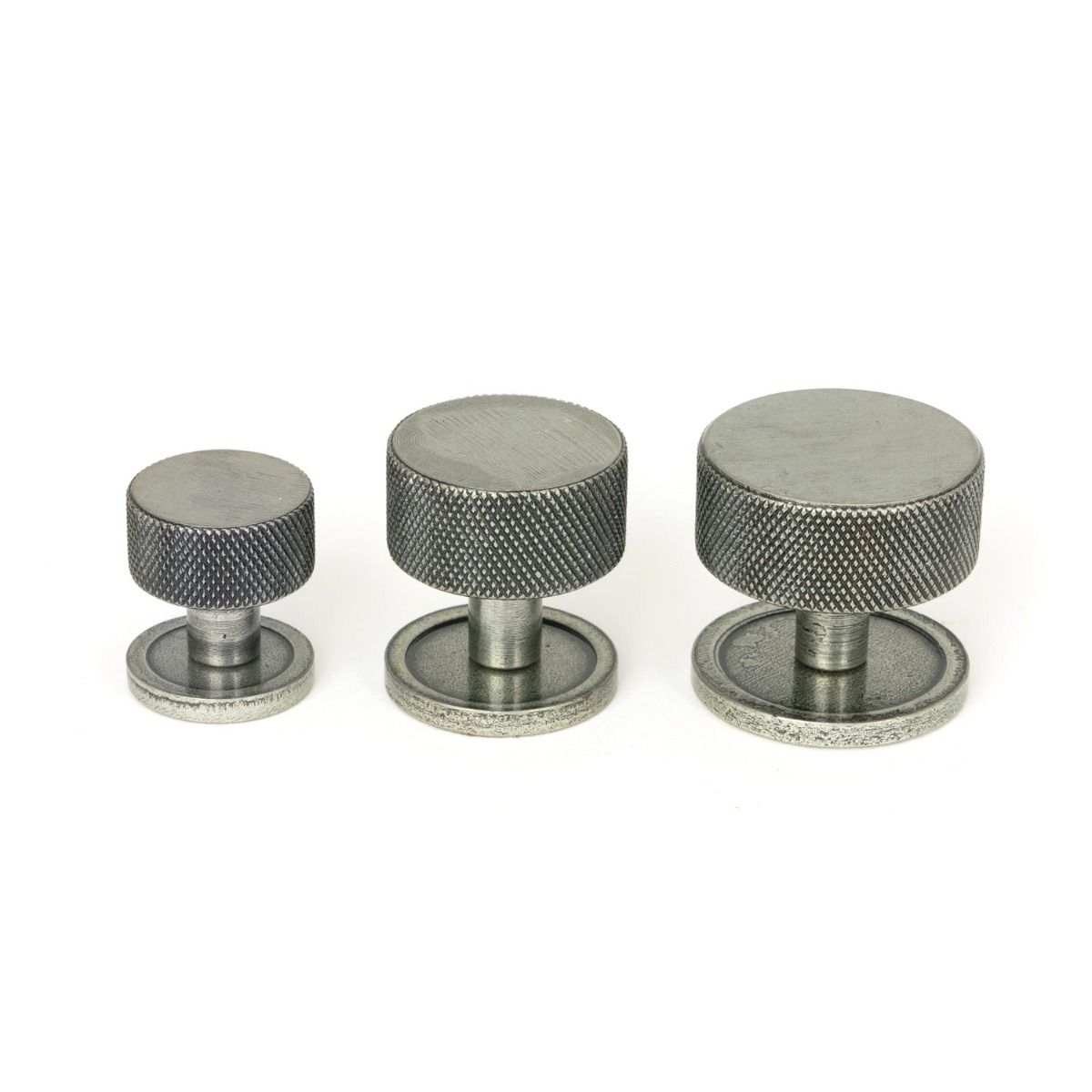 The 25mm Knurled Cabinet Knob on Plain Rose in Pewter Alongside Different Sizes on a White Background
