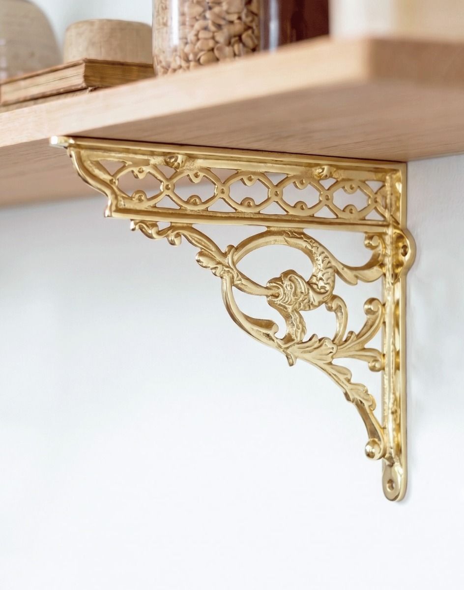 The 29 x 33cm Brass Serpent Design Shelf Bracket Being Used to Support a Wooden DIY Shelf on a White Interior Wall - Digital Illustration 