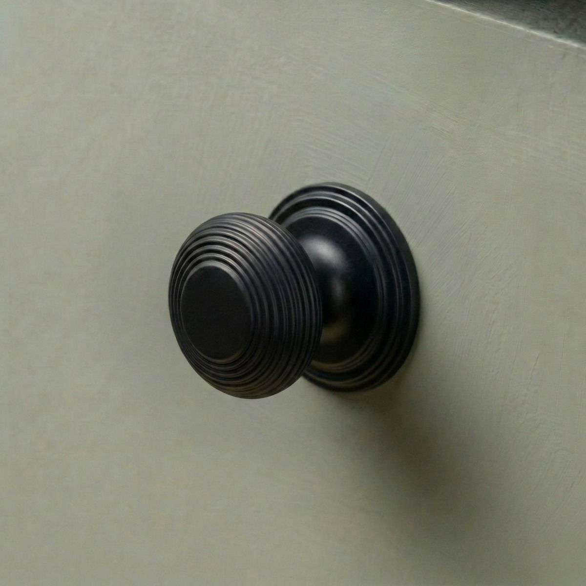 The 30mm "Garrison" Ribbed Beehive Knob in Matt Black Fitted on to a Sage Green Kitchen Cupboard - Digital Illustration