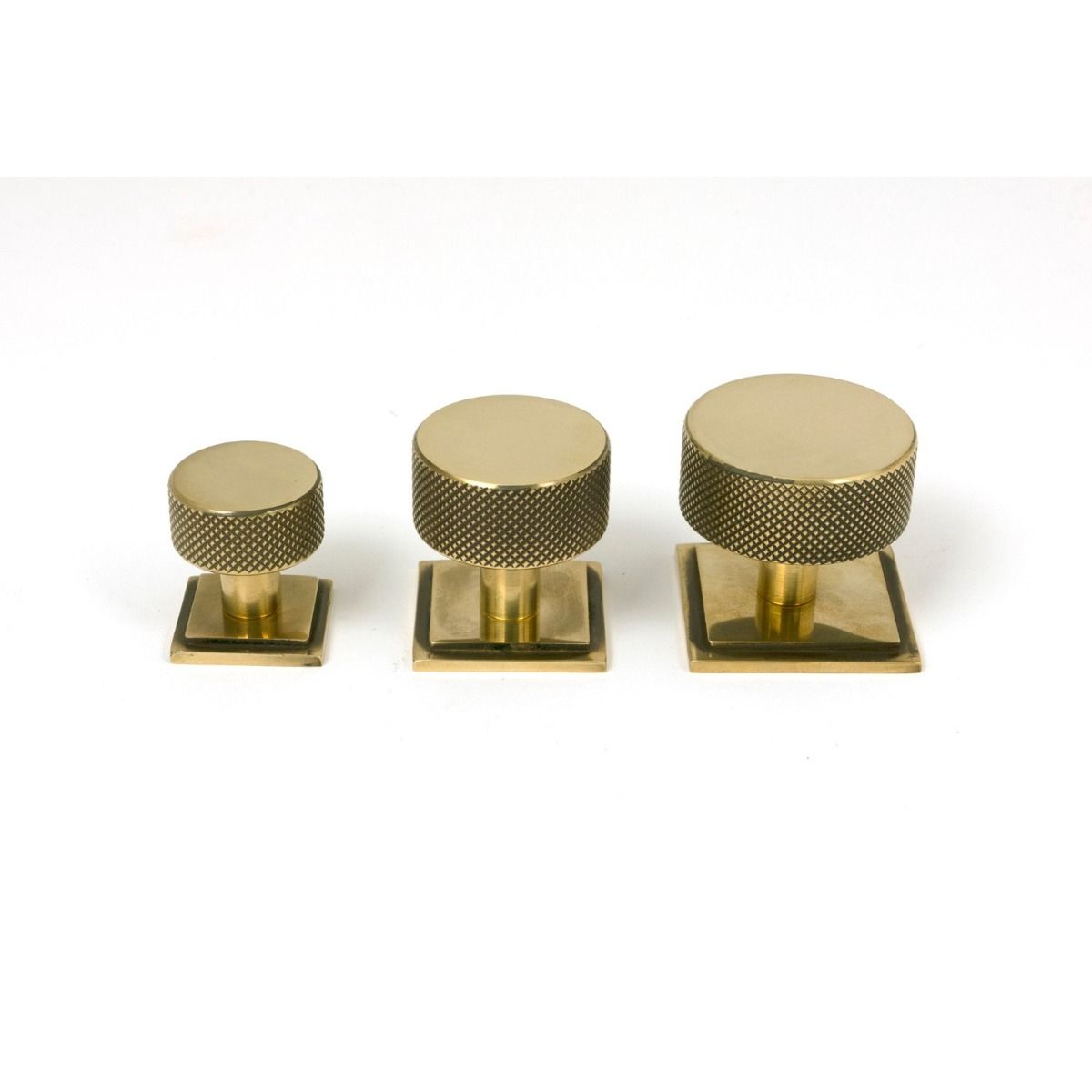 The 32mm Knurled Cabinet Knob on Square Rose in Aged Brass Alongside Different Sizes on a White Background