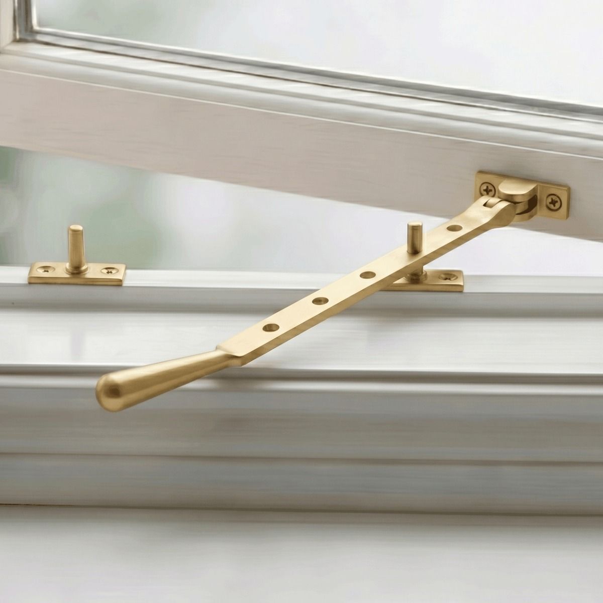 The 335mm 12" Satin Brass Five Pin Window Stay on a White Window Frame in a Country Home - Digital Illustration 