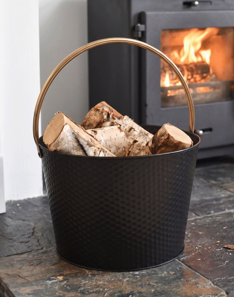 The 38cm Black & Gold Dimpled Steel Log Basket on a Traditional Stone Hearth next to a Lob Burner Stove - Digital Illustration