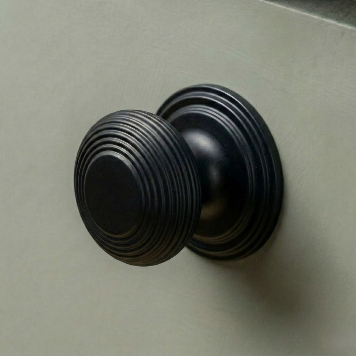 The 40mm "Garrison" Ribbed Beehive Knob in Matt Black Fitted on to a Sage Green Kitchen Cupboard - Digital Illustration