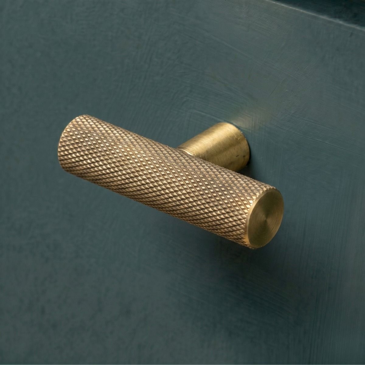 The Aged Brass "Astor" Knurled Industrial T-Bar Cabinet Handle Mounted on a Dark Blue Kitchen Cupboard Drawer - Digital Illustration