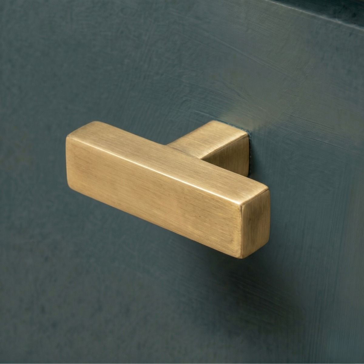 The Aged Brass "Kodiak" Heavyweight Block T-Bar Cabinet Handle Mounted on a Dark Blue Kitchen Cupboard Drawer - Digital Illustration 