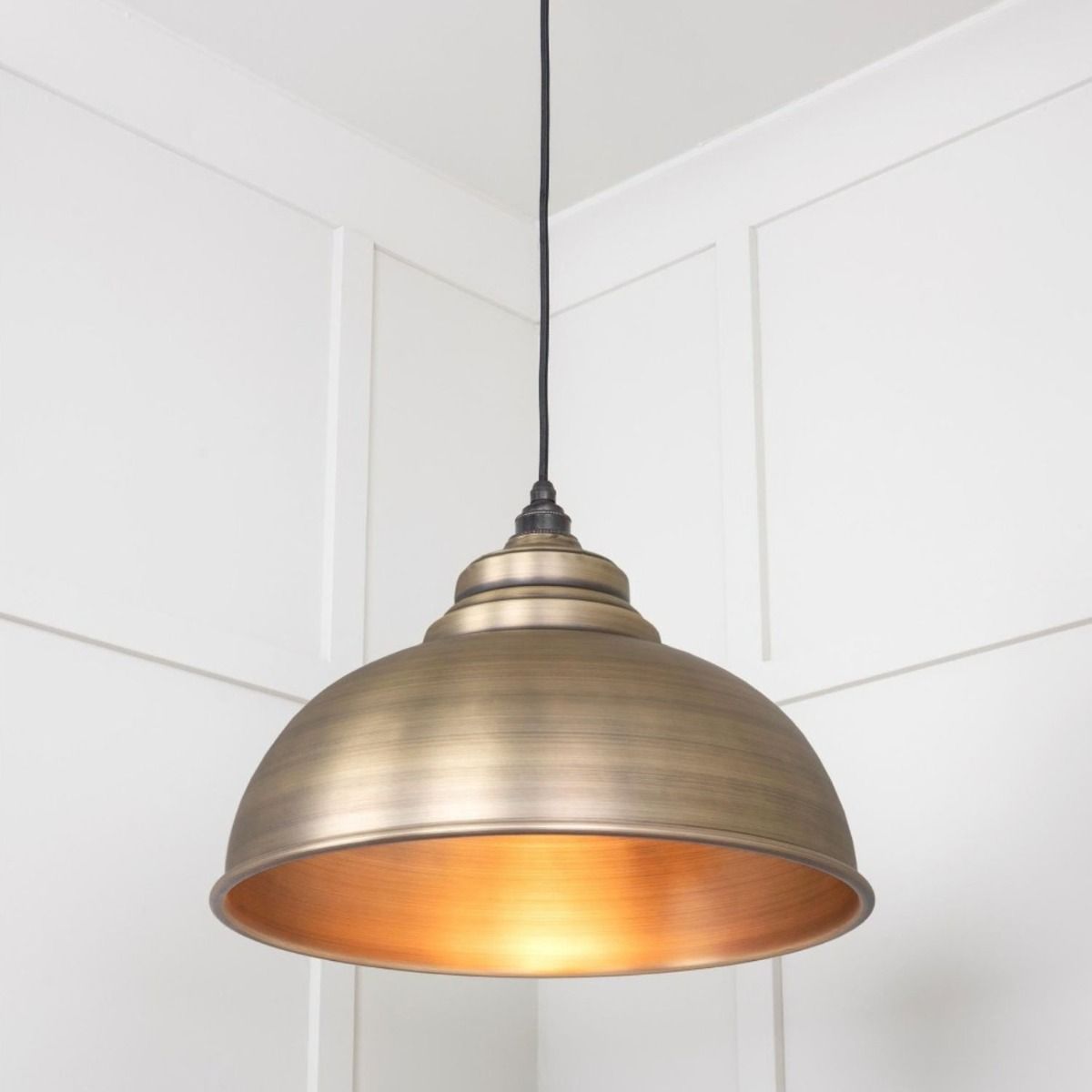 The Arcus Spun Pendant Light in Aged Brass Shown Lit up from a Low Angle
