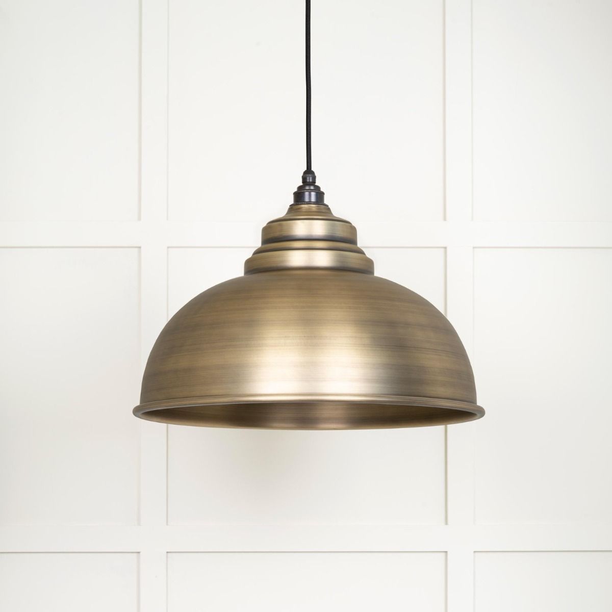 The Arcus Spun Pendant Light in Aged Brass Shown on a White Panelled Background