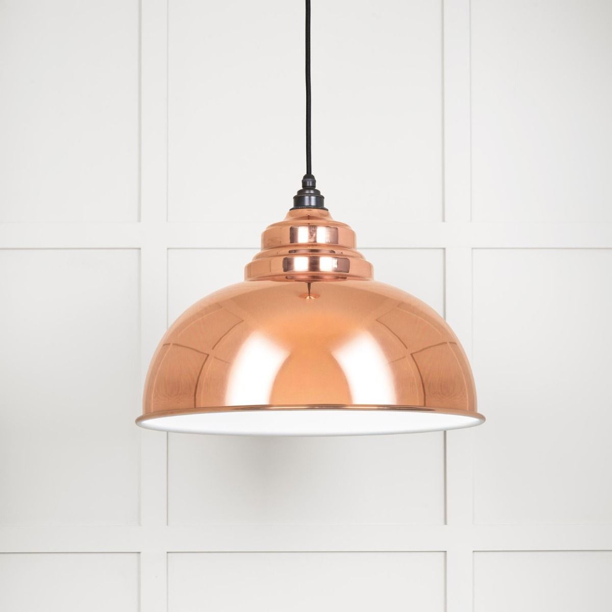 The Arcus Spun Pendant Light in Copper and Glossy White Shown Lit up on a White Panelled Background
