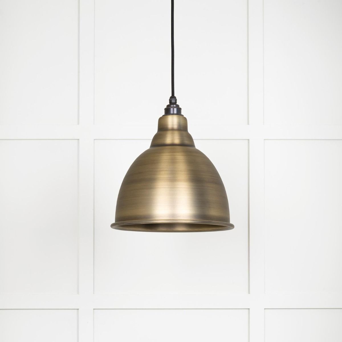 The Aura Dome Pendant Light in Aged Brass Shown with the Light off on a White Panelled Background