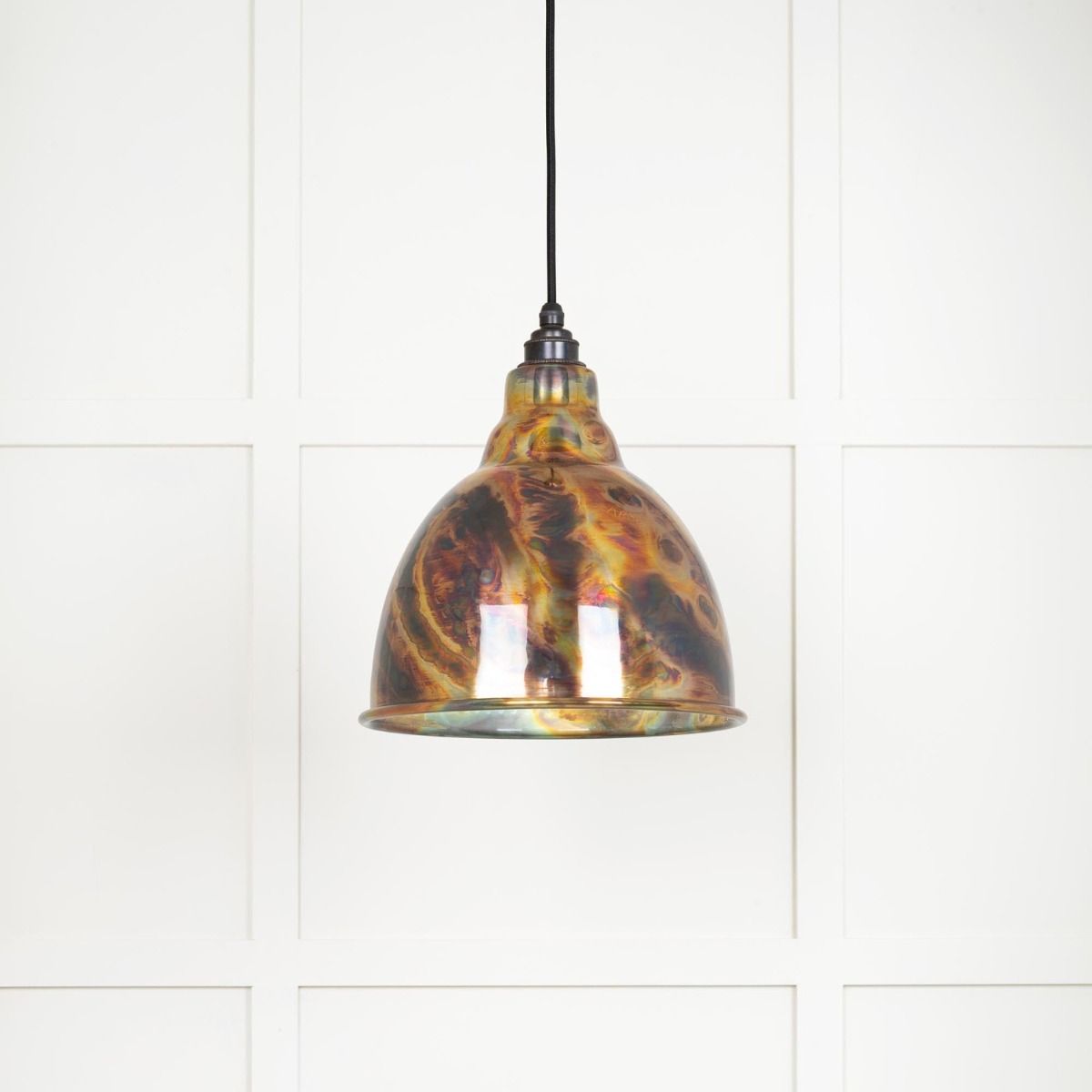The Aura Dome Pendant Light in Burnished Brass Shown Lit up on a White Panelled Background