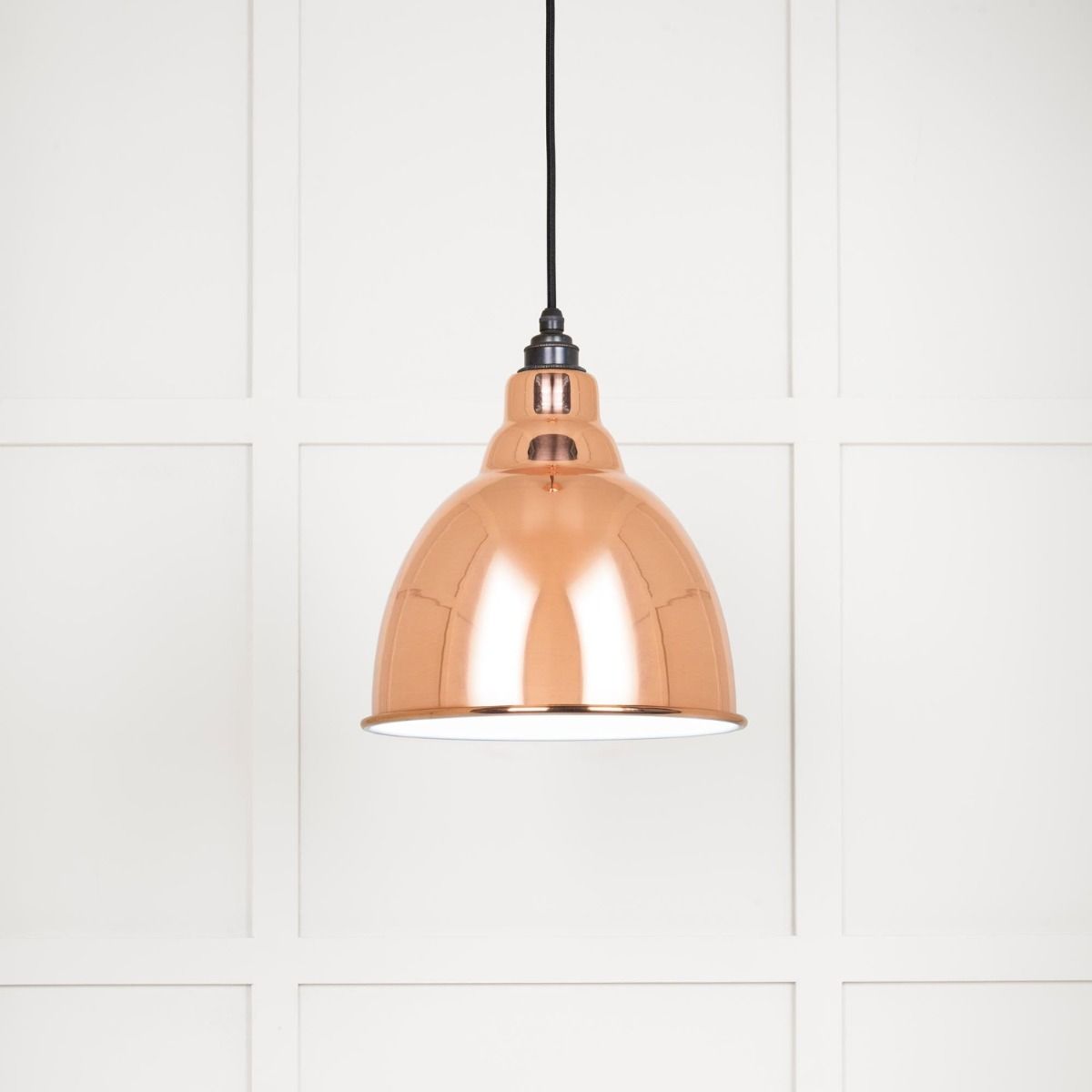 The Aura Dome Pendant Light in Copper and White Gloss Shown Lit up on a White Panelled Background