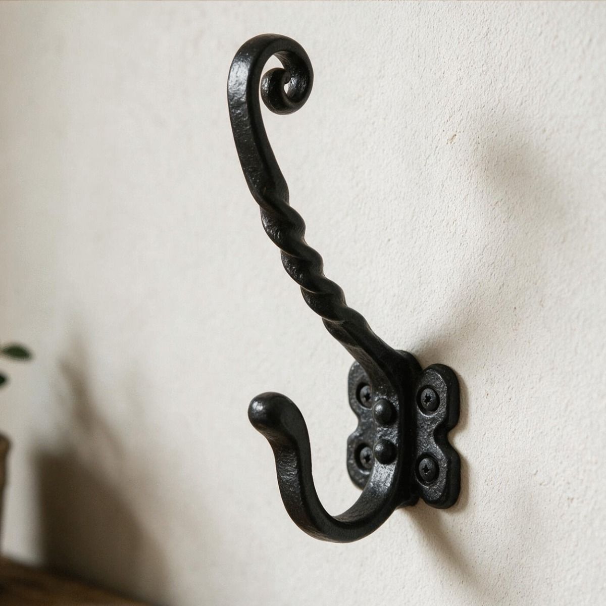 The Black Antique Iron Monkey Tail Twist Design Wall Coat and Hat Hook on a White Wall next to a Timber Shelf - Digital Illustration