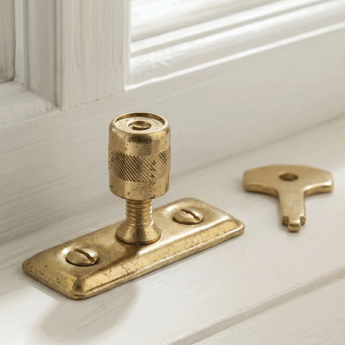 The Casement Stay Locking Pin in Front of a Wooden Window Frame in a Country Home in a Gold Plated Finish - Digital Illustration