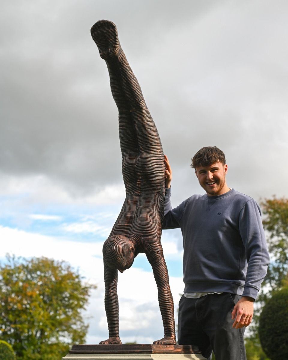The Equilibrium Handstand Garden Sculpture in Copper with a Man Stood Smiling Next to it for Scale