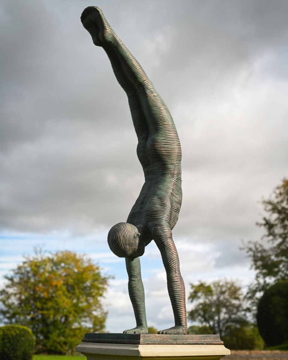 The Equilibrium Handstand Garden Sculpture in Verdigris Displayed as a Garden Centrepiece