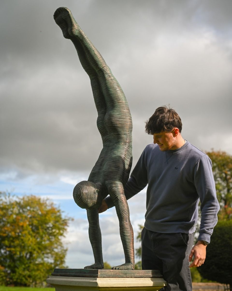 The Equilibrium Handstand Garden Sculpture in Verdigris Shown with a Man Stood Next to the Sculpture