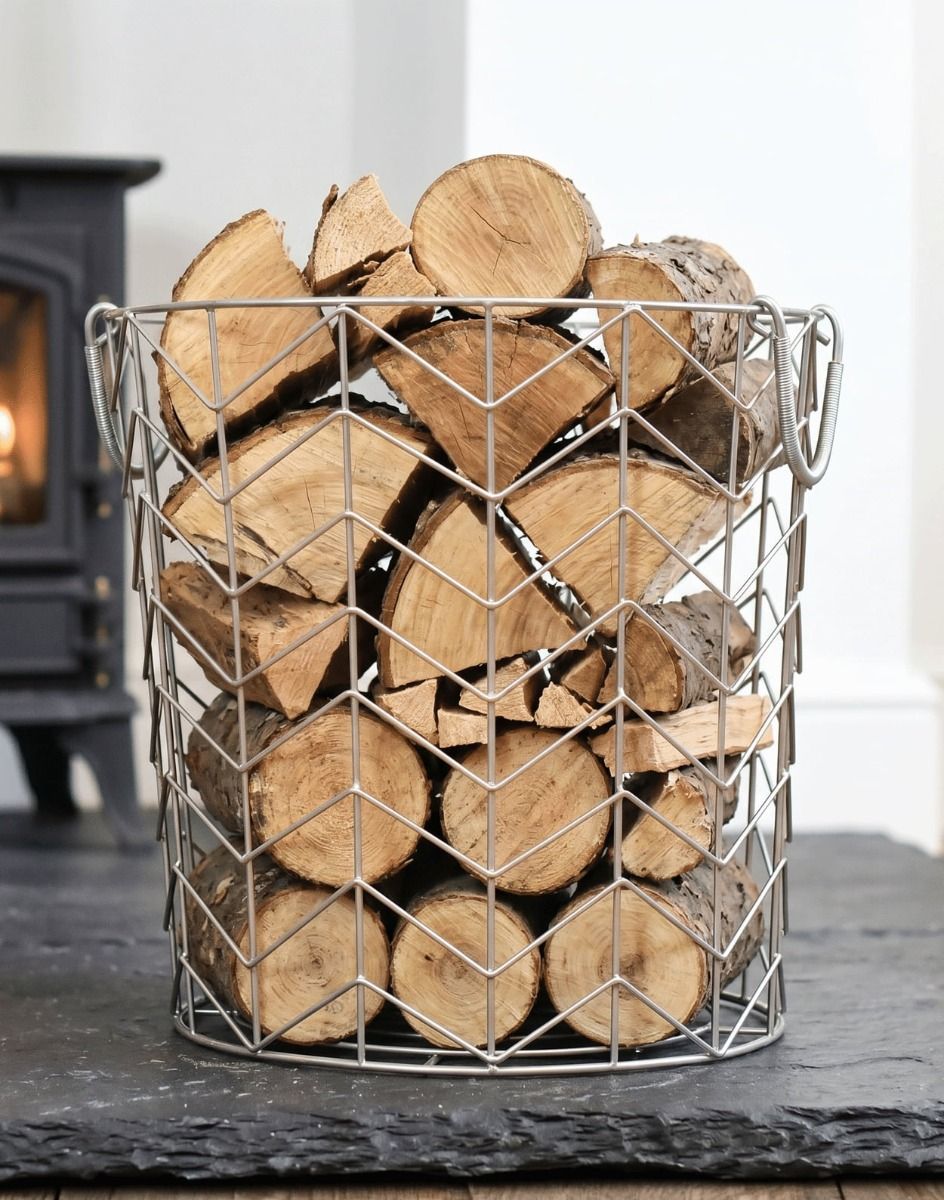 The Medium Pewter Finish Wire Work Log Basket Filled with Logs in Front of a Traditional Log Burner Stove - Digital Illustration