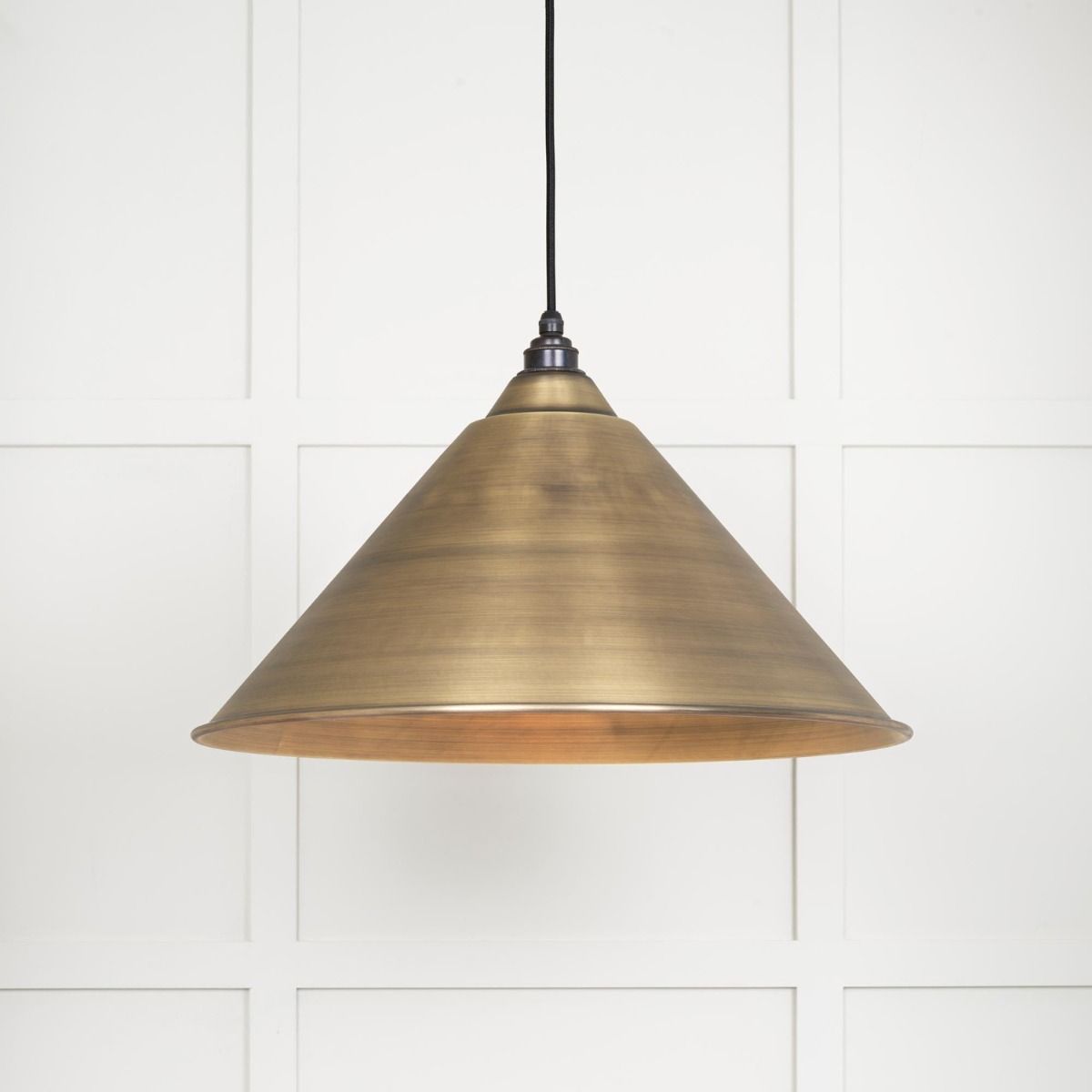 The Nidus Pendant Light in Aged Brass on a White Panelled Background with Light on
