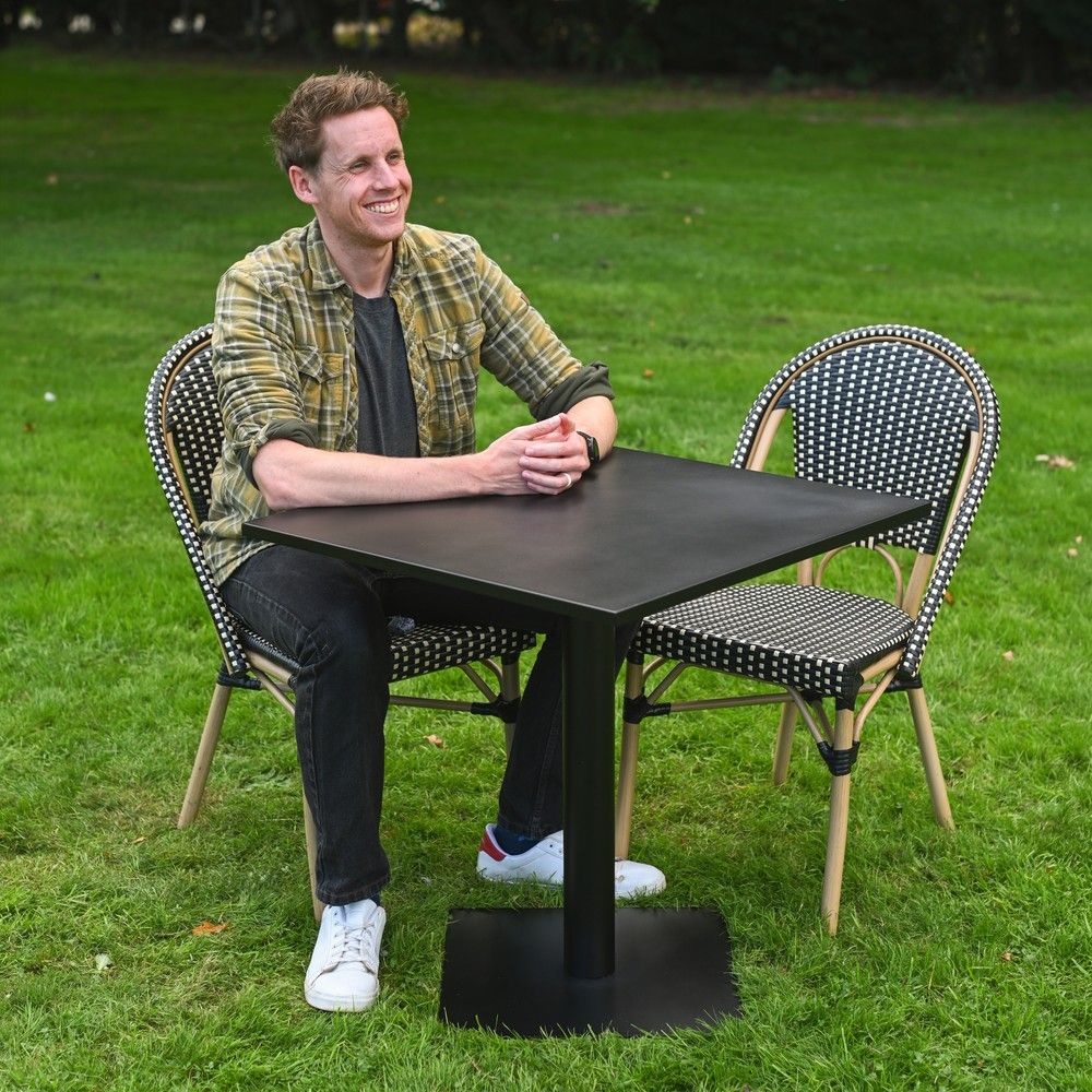 The Parisienne Bistro 2 Seater Outdoor Dining Set in Black and White Shown on. a Garden lawn with a Man Sat at the Table