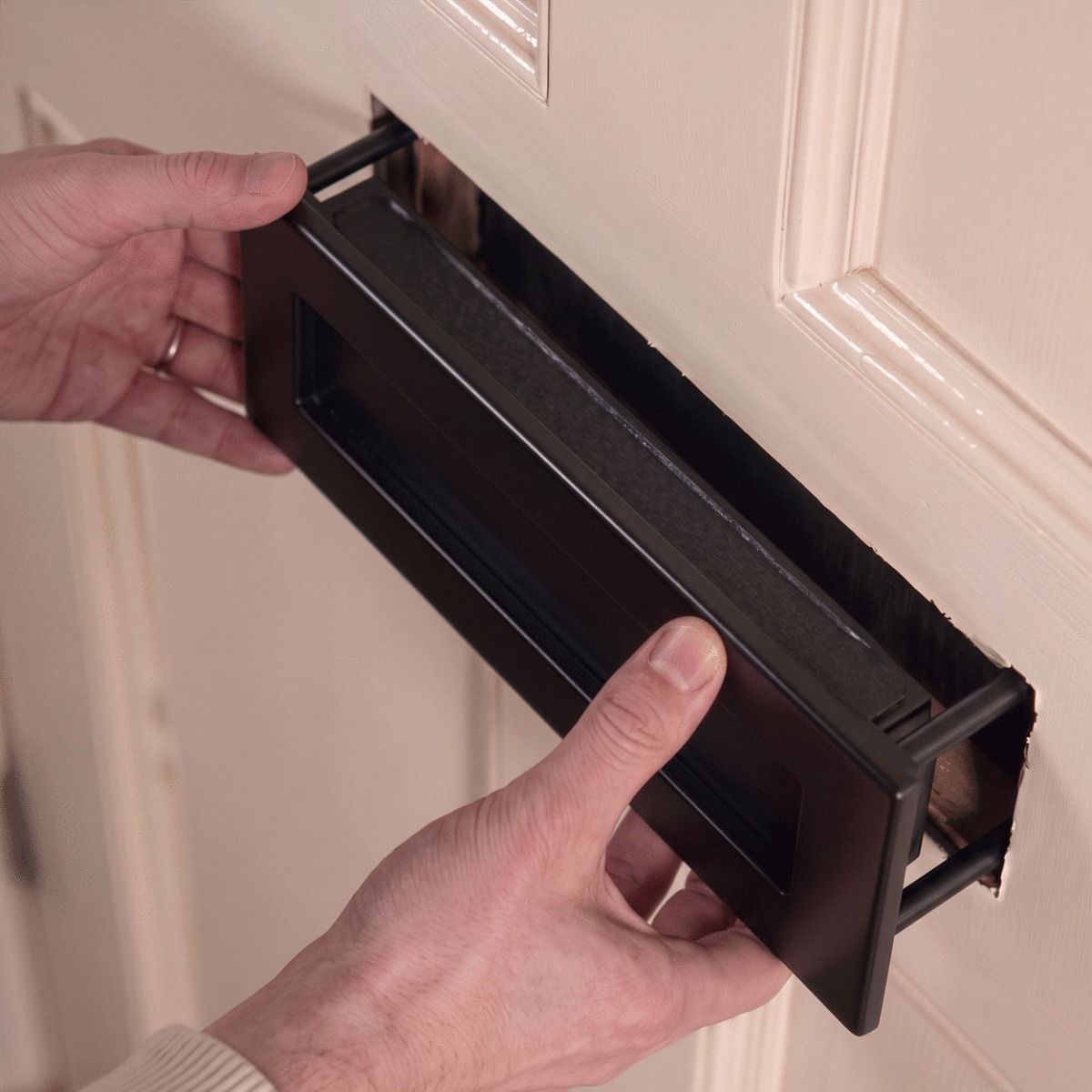 The Traditional 12 Inch Front Door Letter Plate with Antique Period Style Flap in a Black Finish Shown Being Mounted to a Front Door - Digital Illustration 