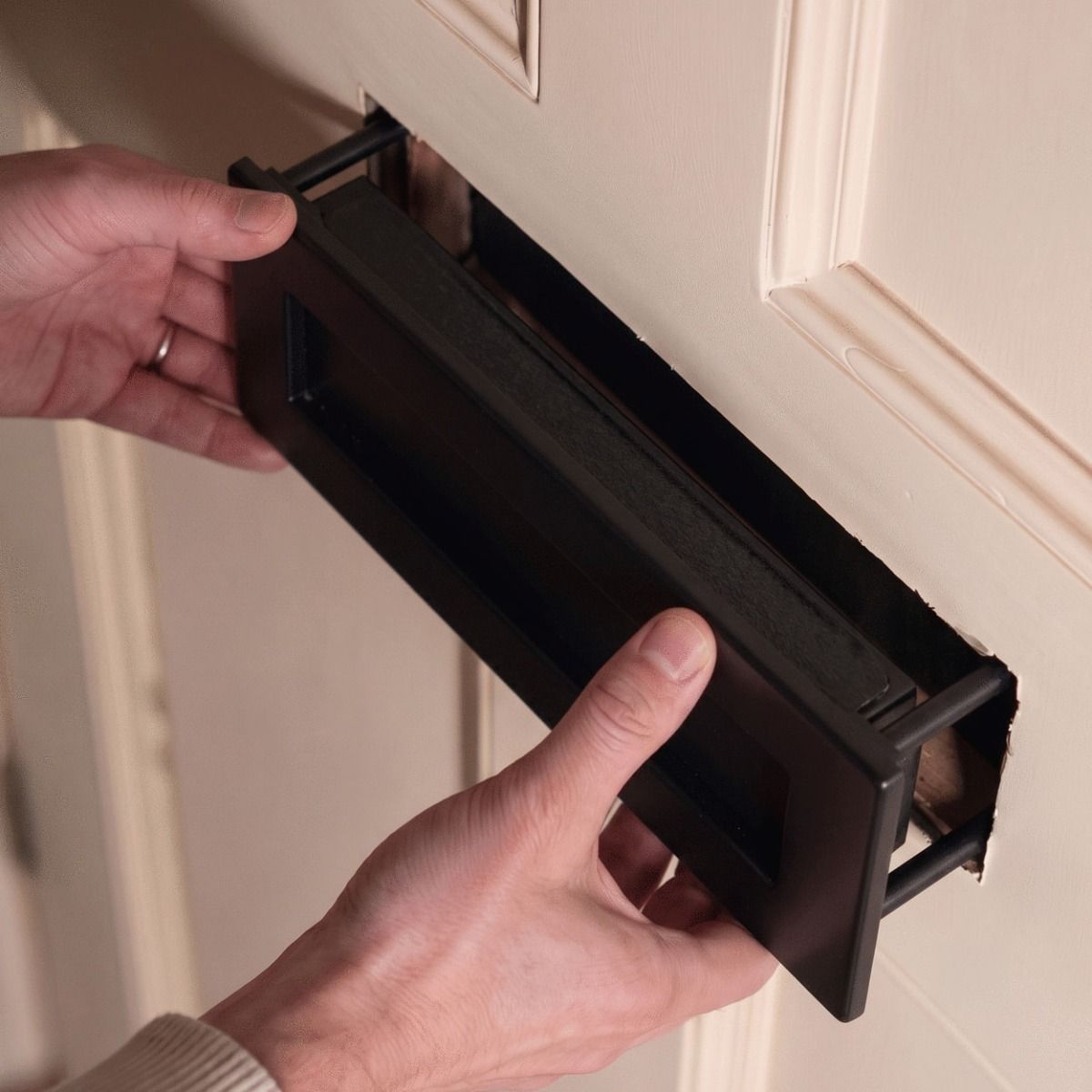 The Traditional 12 Inch Front Door Letter Plate with Antique Period Style Flap in a Matt Black Finish Shown Being Fitted Internally to a Front Door - Digital Illustration 